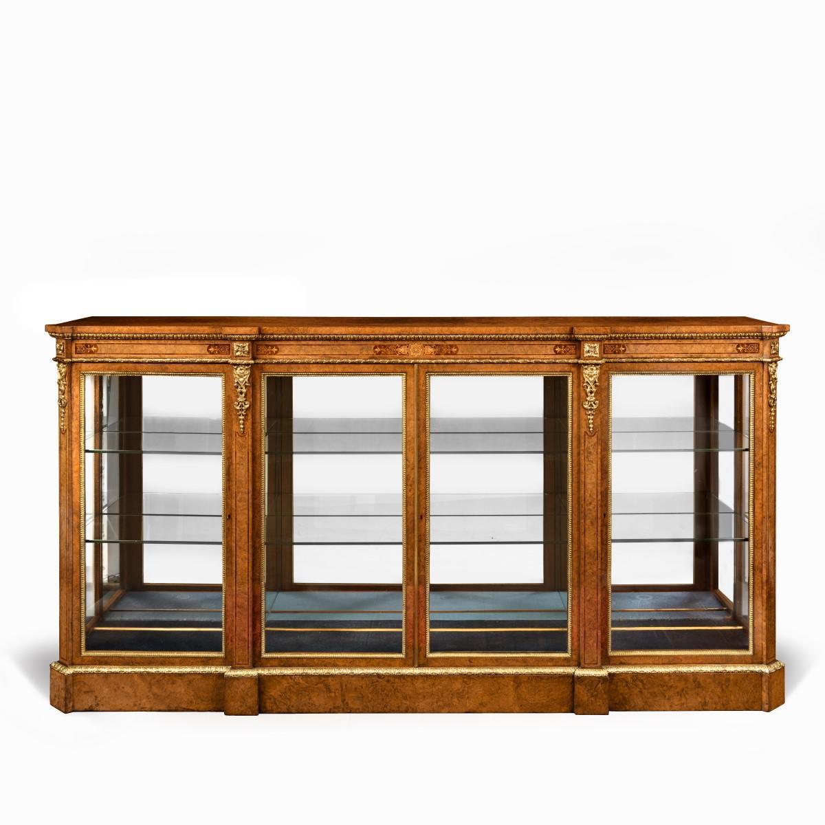 A mid Victorian burr walnut display cabinet, of rectangular breakfront form, with four glazed doors and sides, mirror-backed with two adjustable glass shelves, decorated with delicate boxwood and thoya inlays and fine quality ormolu mounts. English,