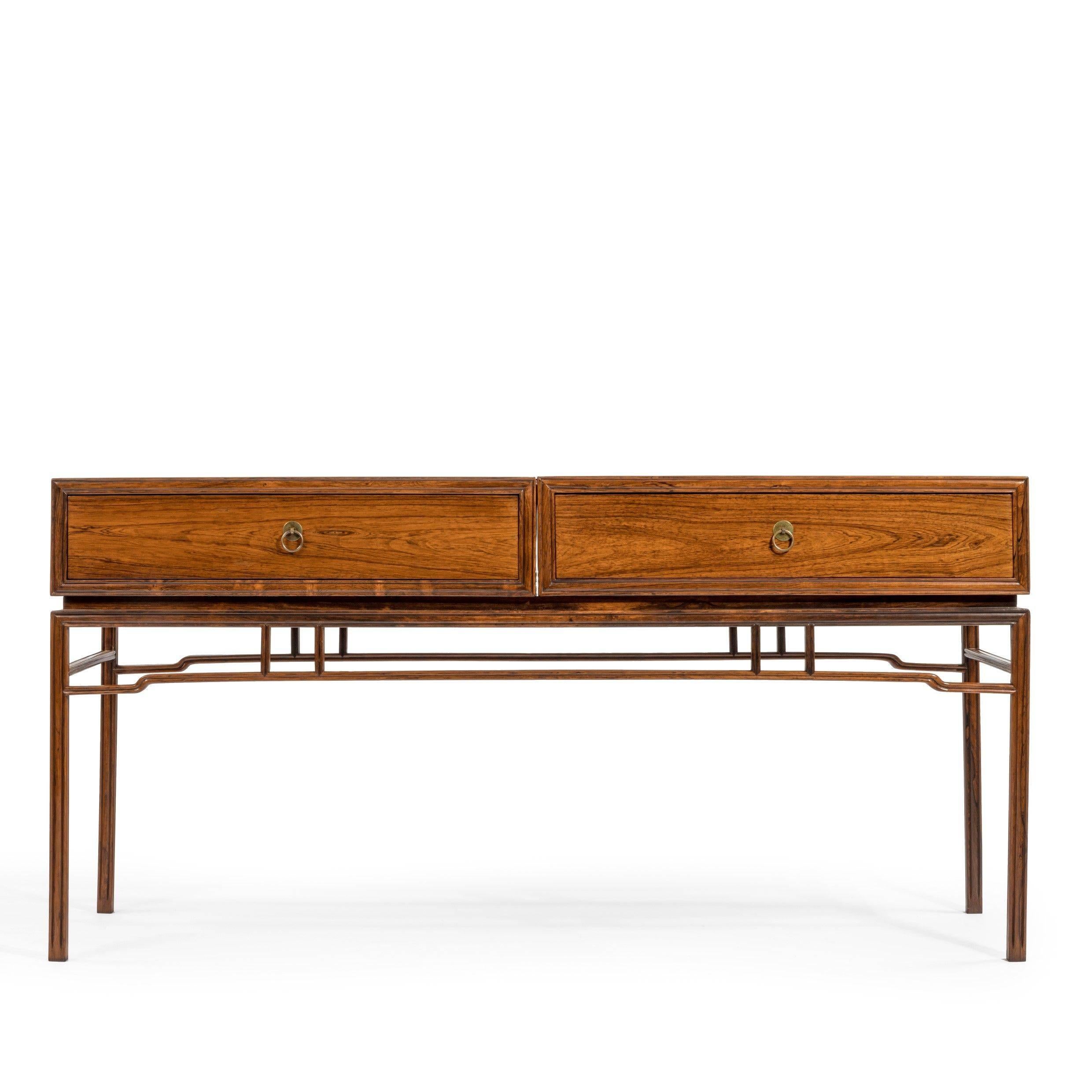 A midcentury hardwood (rosewood) with a Chinese influence.
The two compartments have fitted draws set upon Chinese styled legs and stretchers.

Possibly by Fritz Henning.