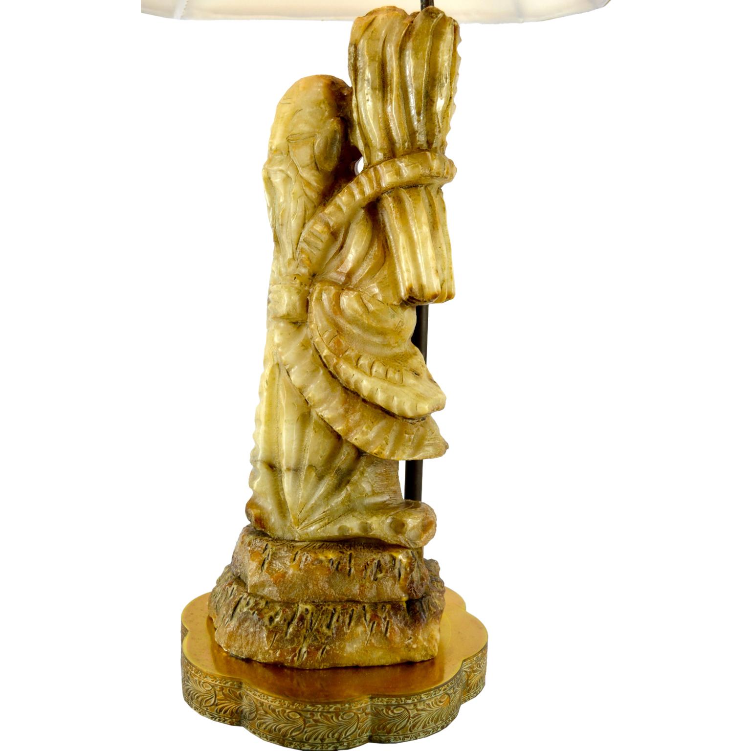 A carved soapstone lamp depicting the Chinese immortal god Shou Xing standing on stone rocks and carrying a wheat sheaf on his back atop two stone ‘rocks’. The figure rests on a later shaped brass base.