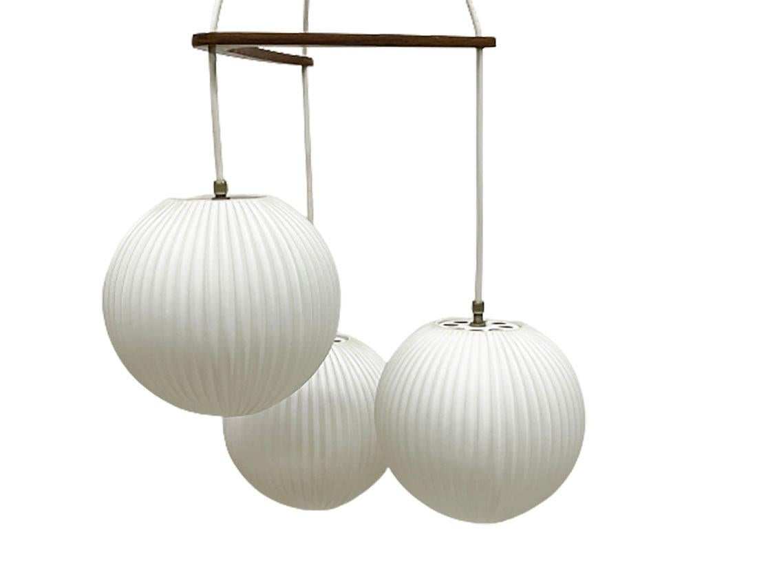 A milk glass pendant lamp by Louis Kalff for Philips.

3 Pleated milk glass shades hanging on a teak wooden boomerang shaped divider
The length from the ceiling is about 76 cm and then the shades are about 20 cm ( approx. 96 cm)
The weight is