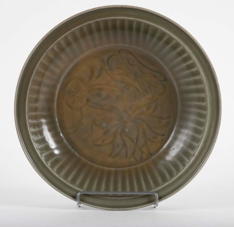 Longquan celadon glazed charger having fluted rim with well centre and incised stylized decoration. Ming dynasty. Underside with burnt orange firing mark otherwise glazed throughout.