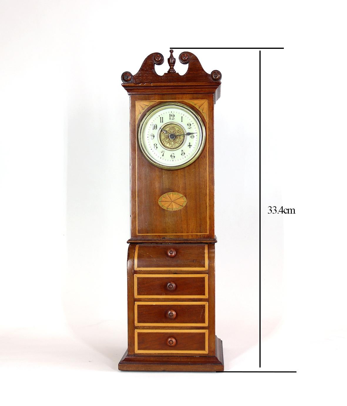A delightful desk clock in the shape of a miniature bureau bookcase with 4 drawers. Fitted with a french eight day timepiece with a platform escapement the cream arabic chapter ring surrounding a filigree centre. The case in a sheraton revival style