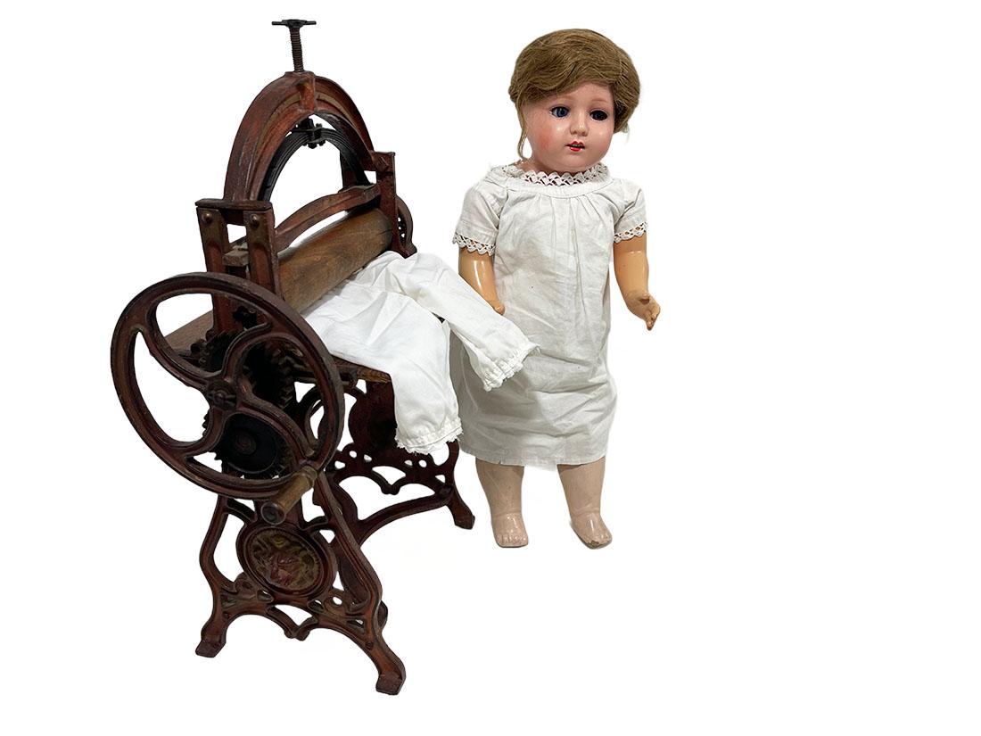 A miniature cast iron linen press with Schildkröt doll, 1890-1900

An antique miniature mangle linen press, circa 1890-1900, made of cast iron with 2 wooden shelves and wooden rollers. The linen press is working, rotating on the wheel with springs