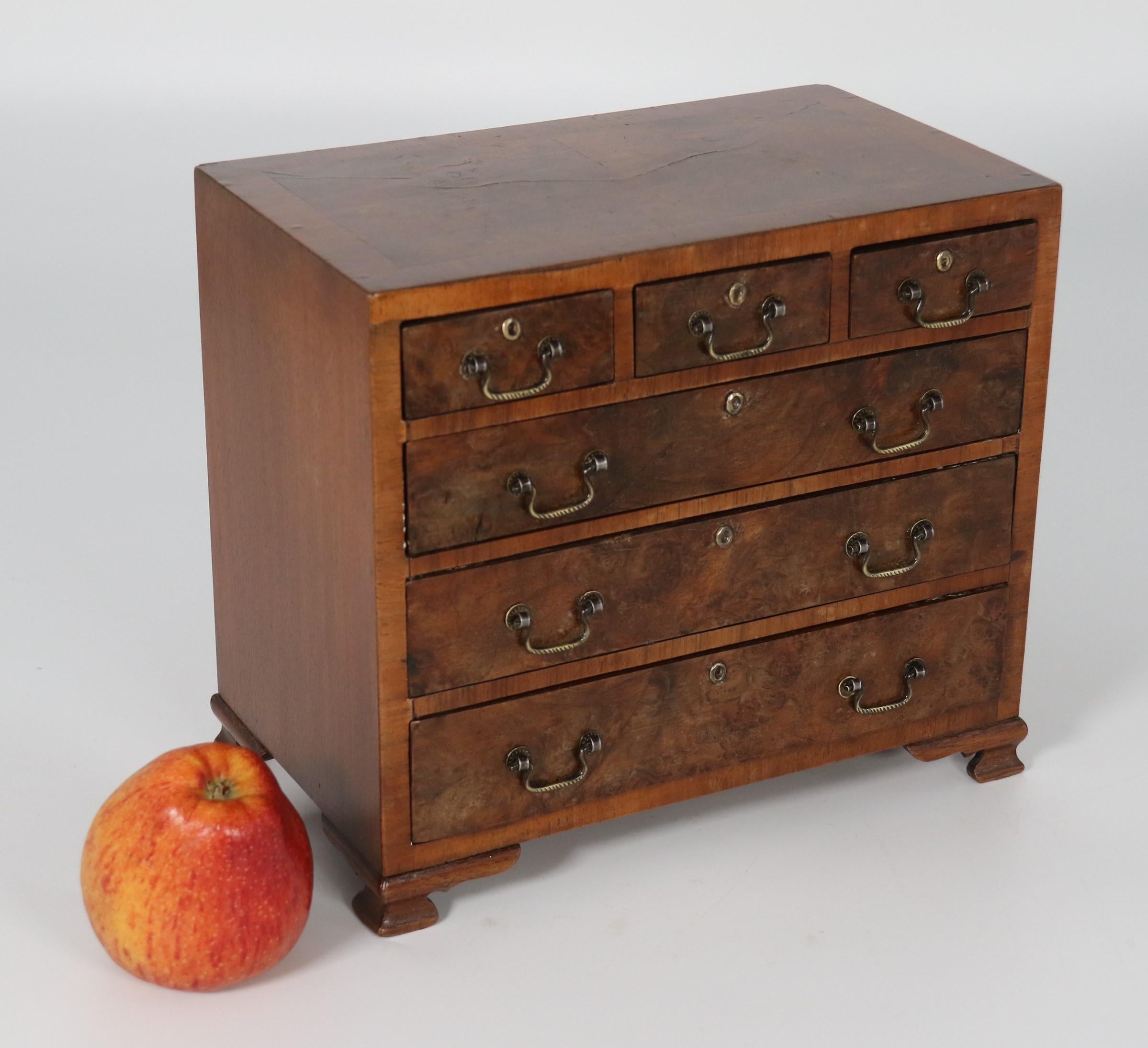 
This most pleasing and rare small miniature apprentice type chest of drawers is beautifully handmade and veneered in burr walnut with a book matched top finished with a cross banded edge in straight grain walnut which matches the parting rails and