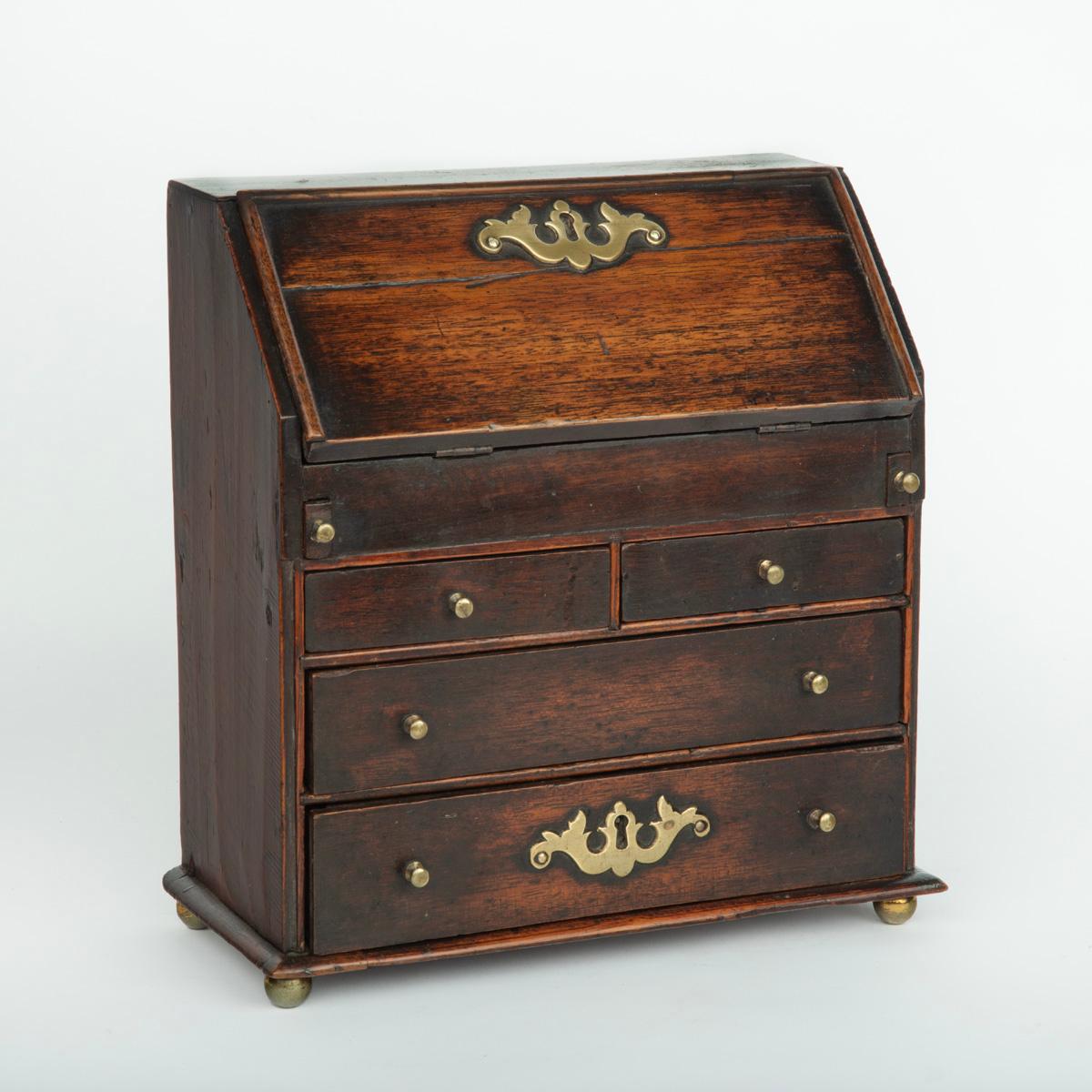 A miniature George III mahogany bureau apprentice piece, of rectangular form with a fall front and fitted pine interior with an arrangement of small drawers and pigeon holes, all above two short and two graduated long drawers, raised on brass bun