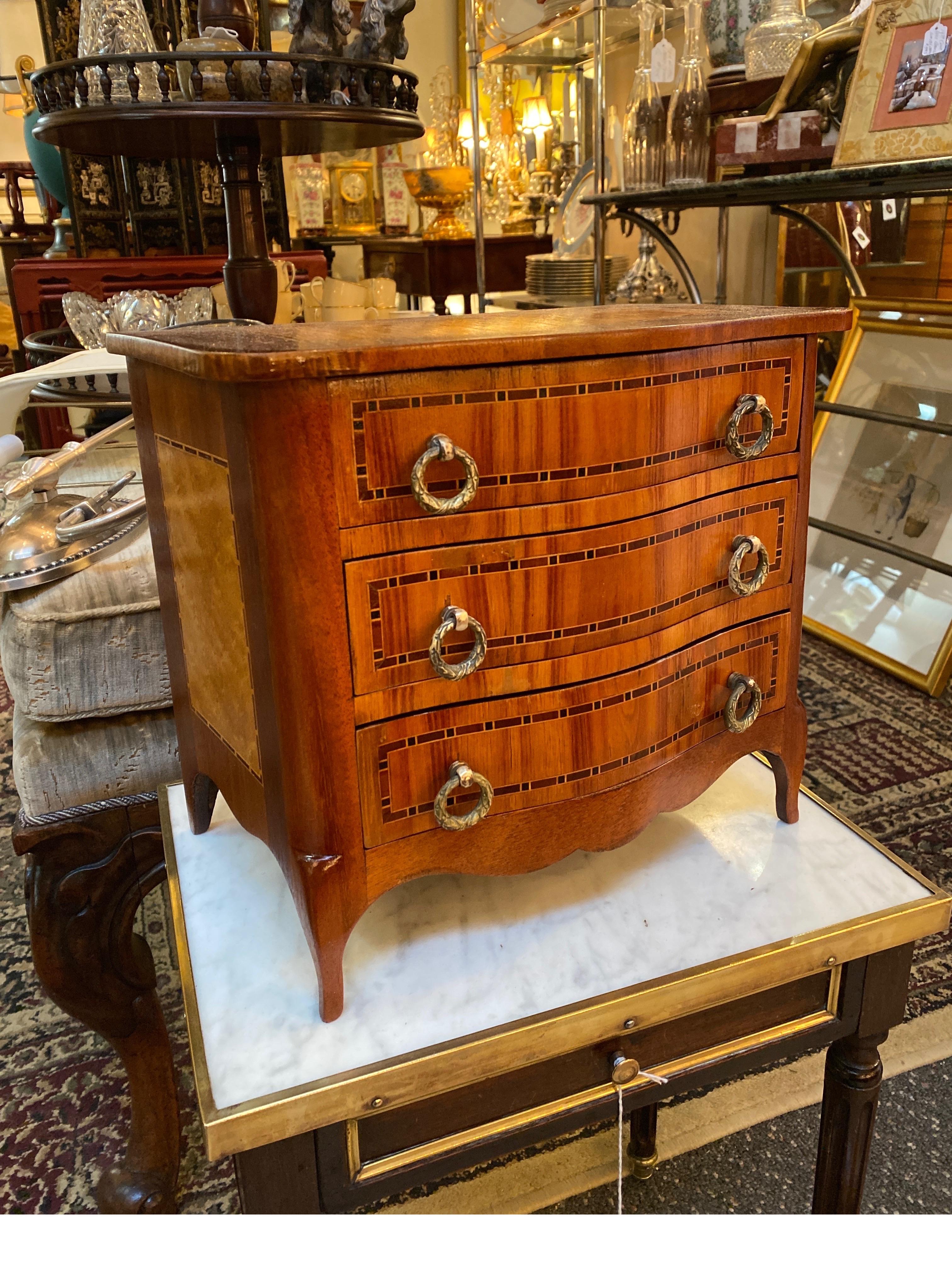 A beautifully made fully functional miniature chest of drawers. This three-drawer chest of mahogany with inlaid panels of satinwood and pencil inlay. Only 11 inches tall, this chest is a table top version of a standard cast with cast brass handles