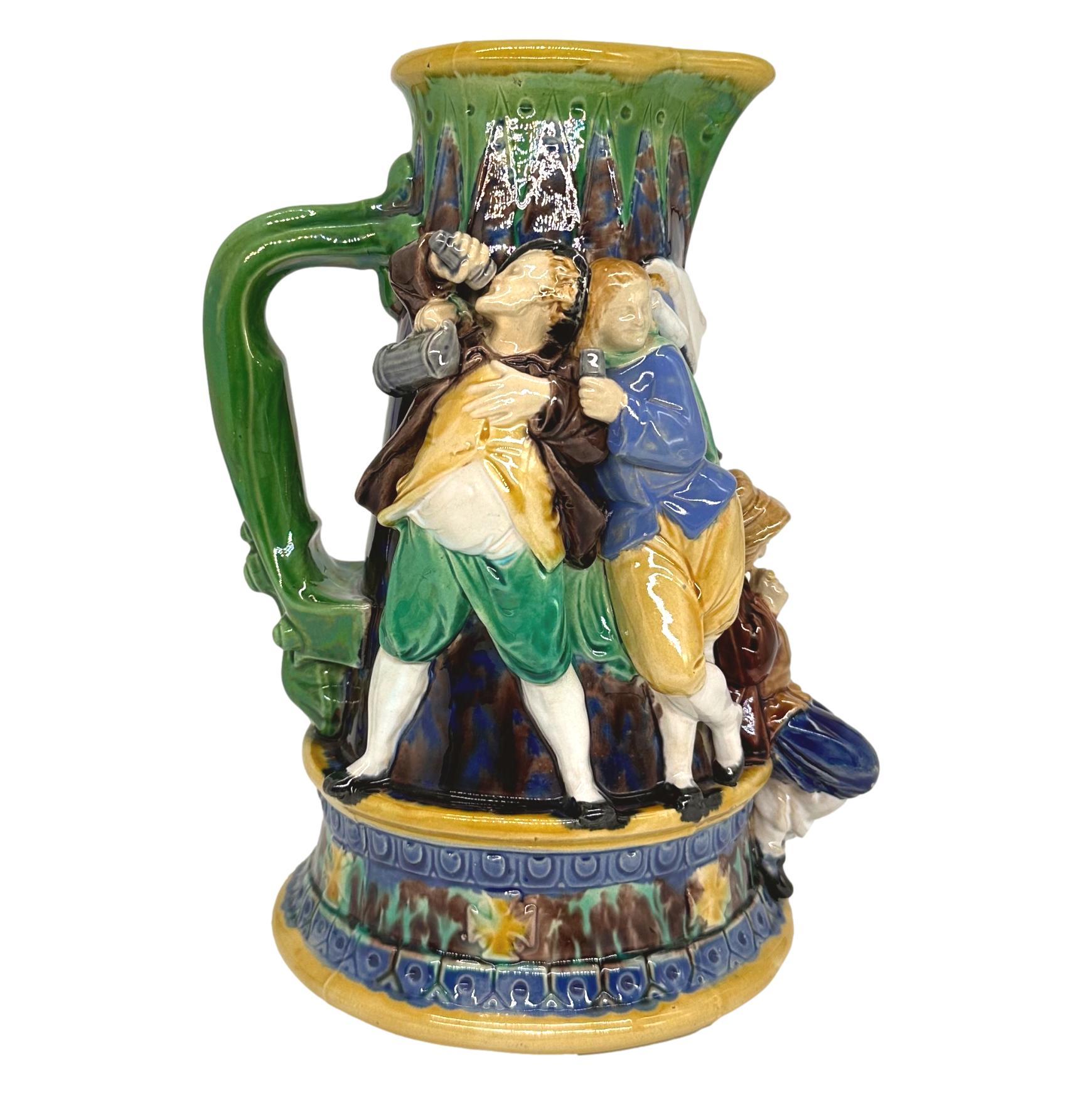 An Early Minton Majolica 'Tavern' Ale Jug, formed as a tapering medieval flagon, the figures molded in high relief and applied, depicting a man and woman dancing, a seated figure with a pipe, and two drunk men on a cobalt blue and brown mottled