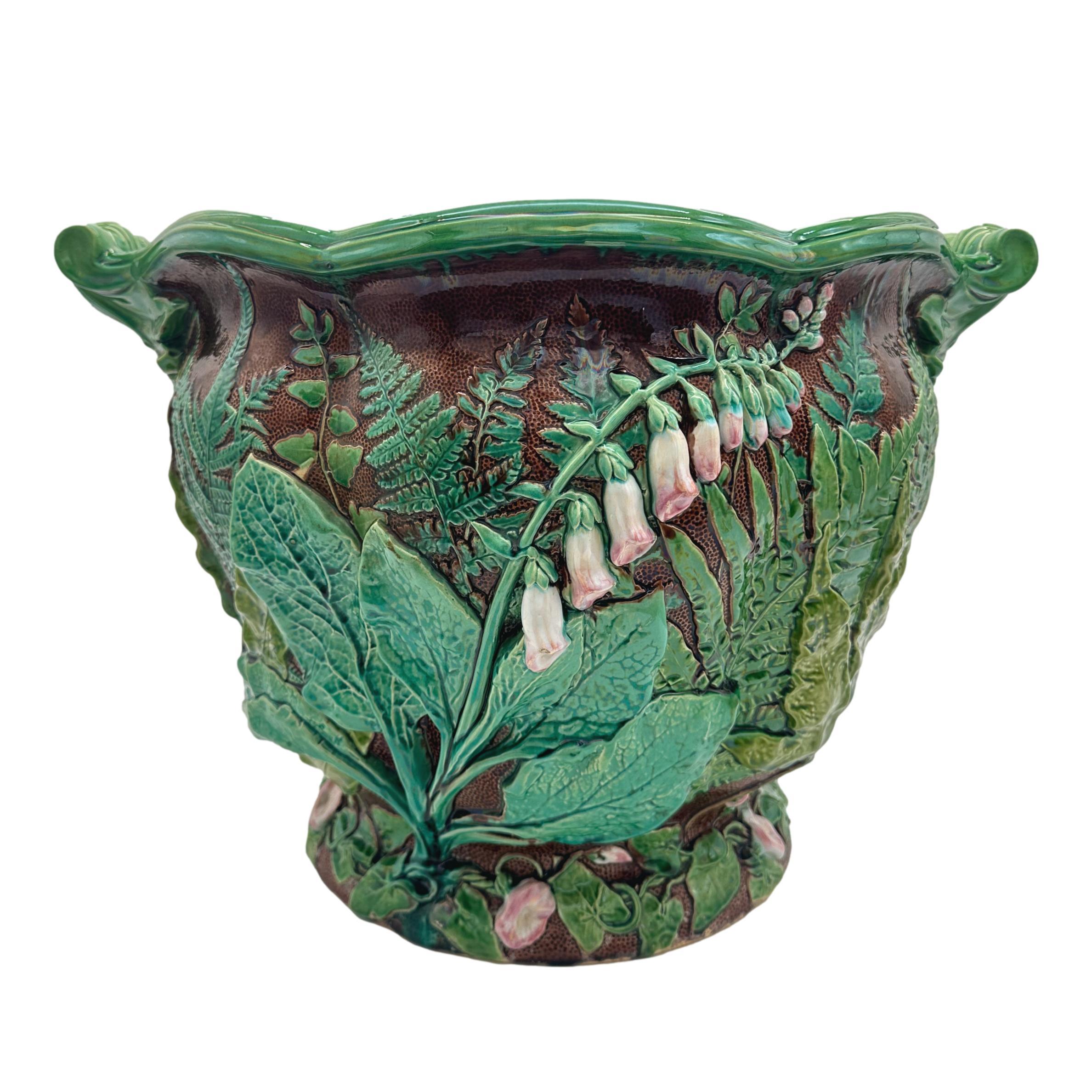 A Minton Majolica Foxglove Jardiniere and Stand, molded with naturalistic trompe l'oeil foxgloves, ferns, and morning glories on a rustic ground, with a shaped oval rim and foliate-scroll handles, the reverse glazed in pink with impressed marks: