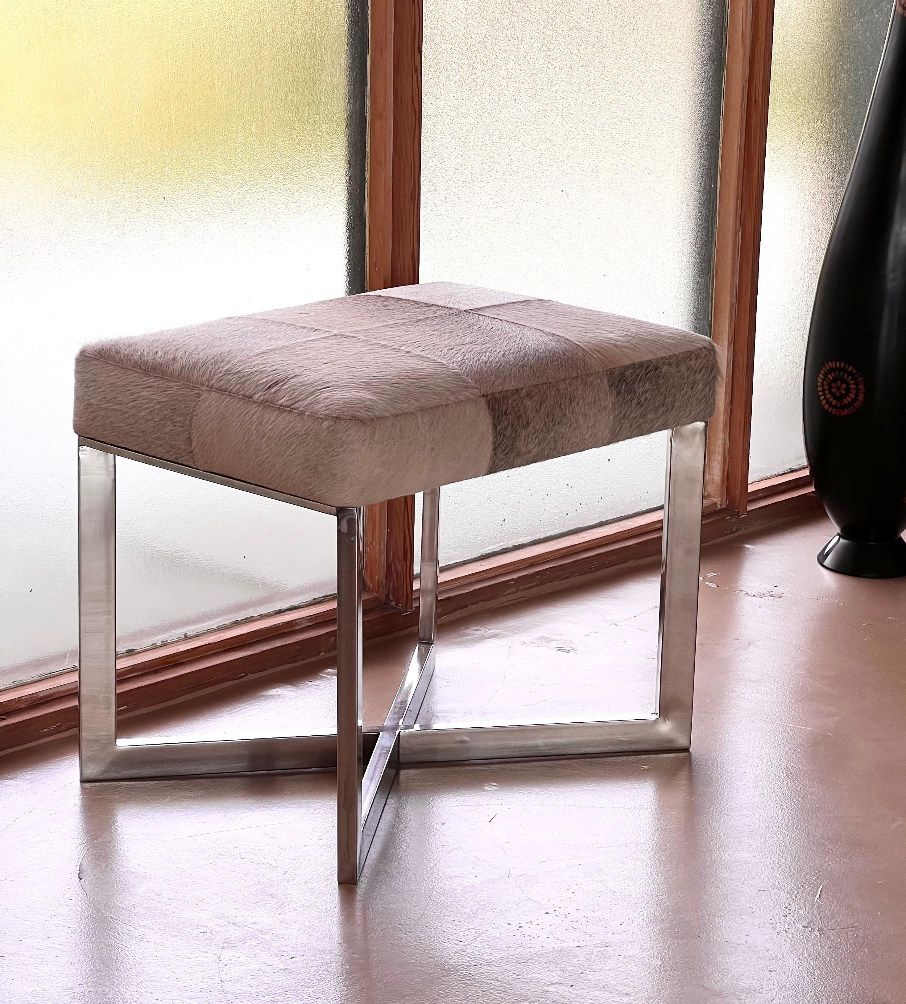 A modernist chrome and cowhide ottoman or stool, probably late 20th century or early 21st century. Likely a mid century modern reproduction. 