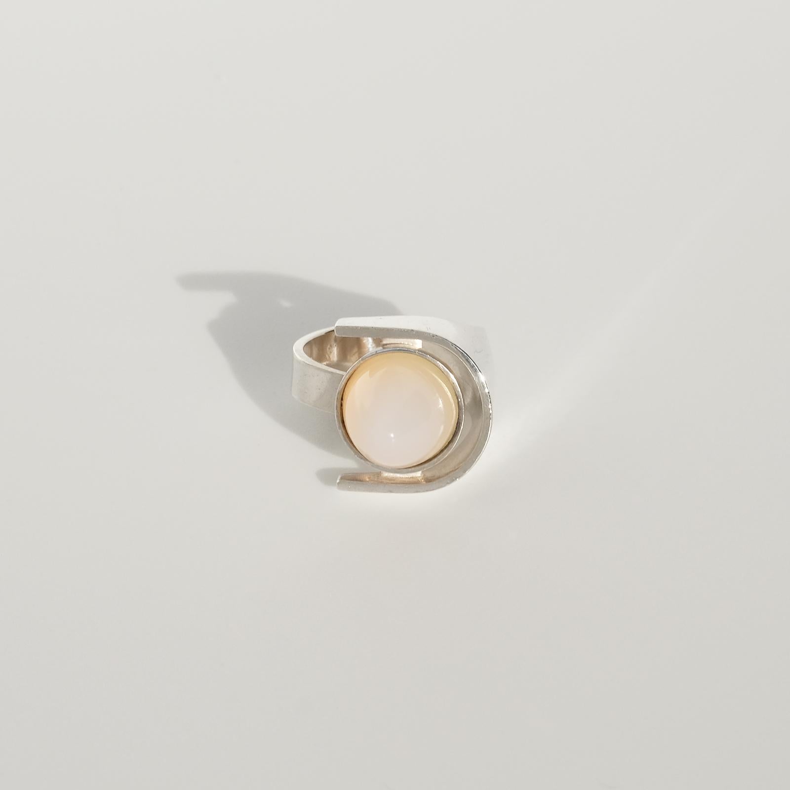 This modernist sterling silver ring is adorned with a high cabochon cut moonstone. The beautiful moonstone changes from blue-white transparent to light yellow depending on the light.

The shape of this ring can be described as embracing and out of