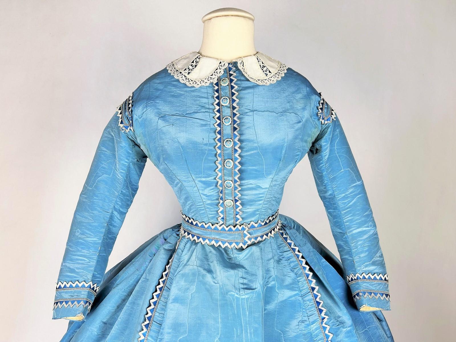 CIRCA 1865
Frankreich Zeit des Zweiten Kaiserreichs
Ein Nachmittagskleid mit Schleppe und großer vorspringender Krinoline, Mieder und Rock aus blauer Seide 