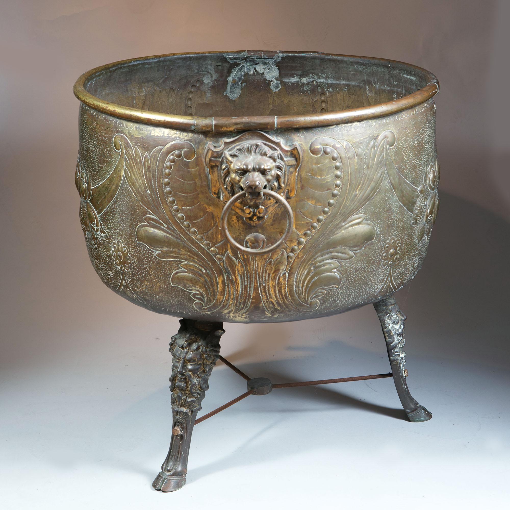 A monumental 19th century repoussé brass log bin, Dutch c.1860, lion mask ring handles to either side, supported on three legs with flamboyant lion masks above neat hoof feet, iron rod stretchers beneath linked by central ring, strikingly exuberant