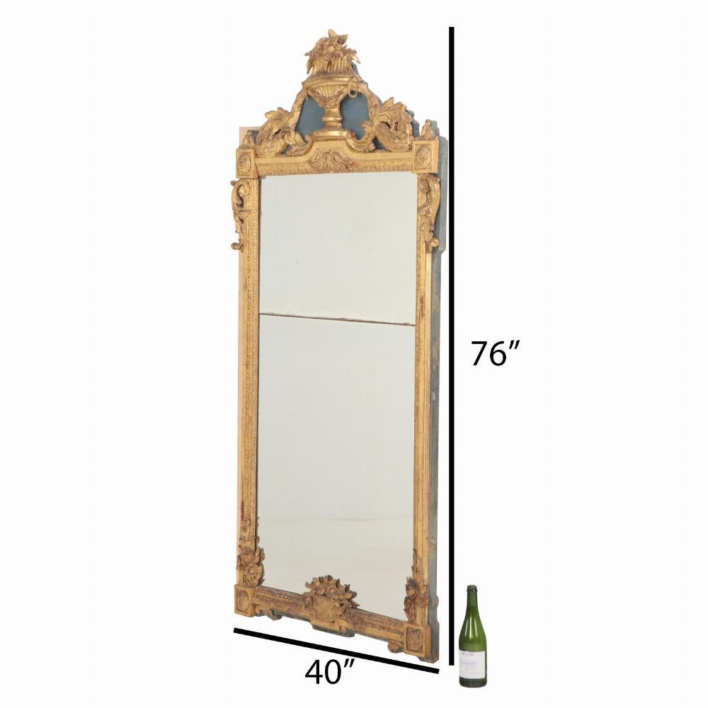 Splendidamente intagliato, questo specchio dipinto, in legno dorato e gesso è ricco di dettagli. Un'urna floreale intagliata e fiancheggiata da una ghirlanda fogliare si trova in cima alla cornice rettangolare ad angolo. Ogni angolo della cornice è