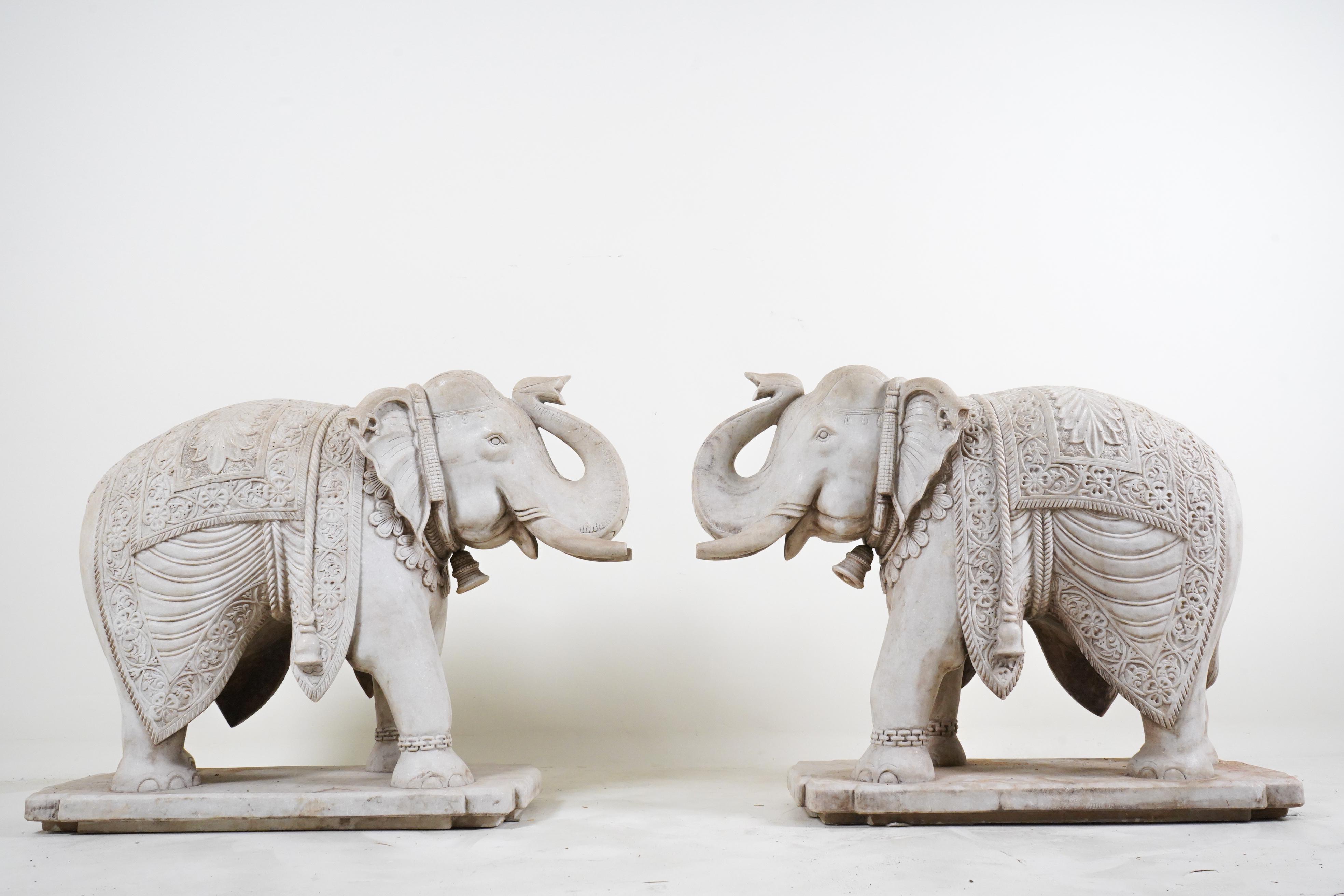 This is an exquisitely carved pair of  Indian marble elephants. Standing foursquare,  these magnificent creatures embody elegance and power. Sculpted from fine white marble, their intricate details and lifelike features captivate the beholder's
