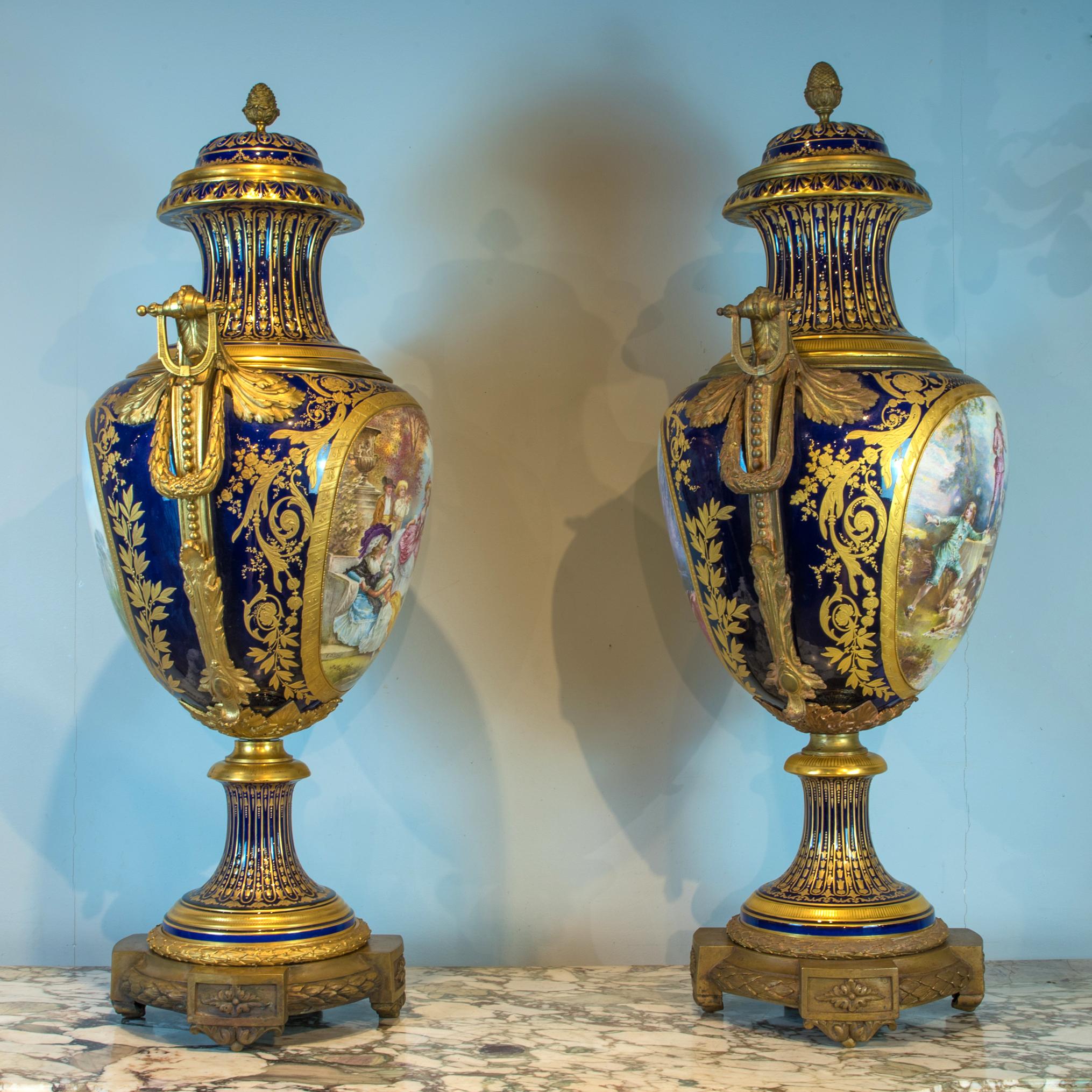 Hand painted with scenes of a chateau landscape and courtly couples in a garden, signed 'E. Collot', on a gilt and cobalt ground, gilt-bronze acanthus swag handles, base and foliate knopped cover. The other painted reserve in the Rococo manner,