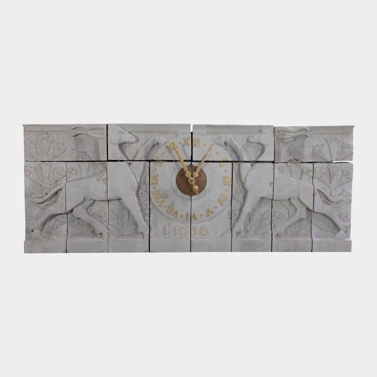 Une horloge murale en pierre de taille monumentale attribuée à Esmond Burton. En 12 pièces avec des feuillages stylisés et deux gazelles opposées, l'horloge en bronze au centre avec des chiffres romains dorés. Cette horloge a été retirée du bâtiment