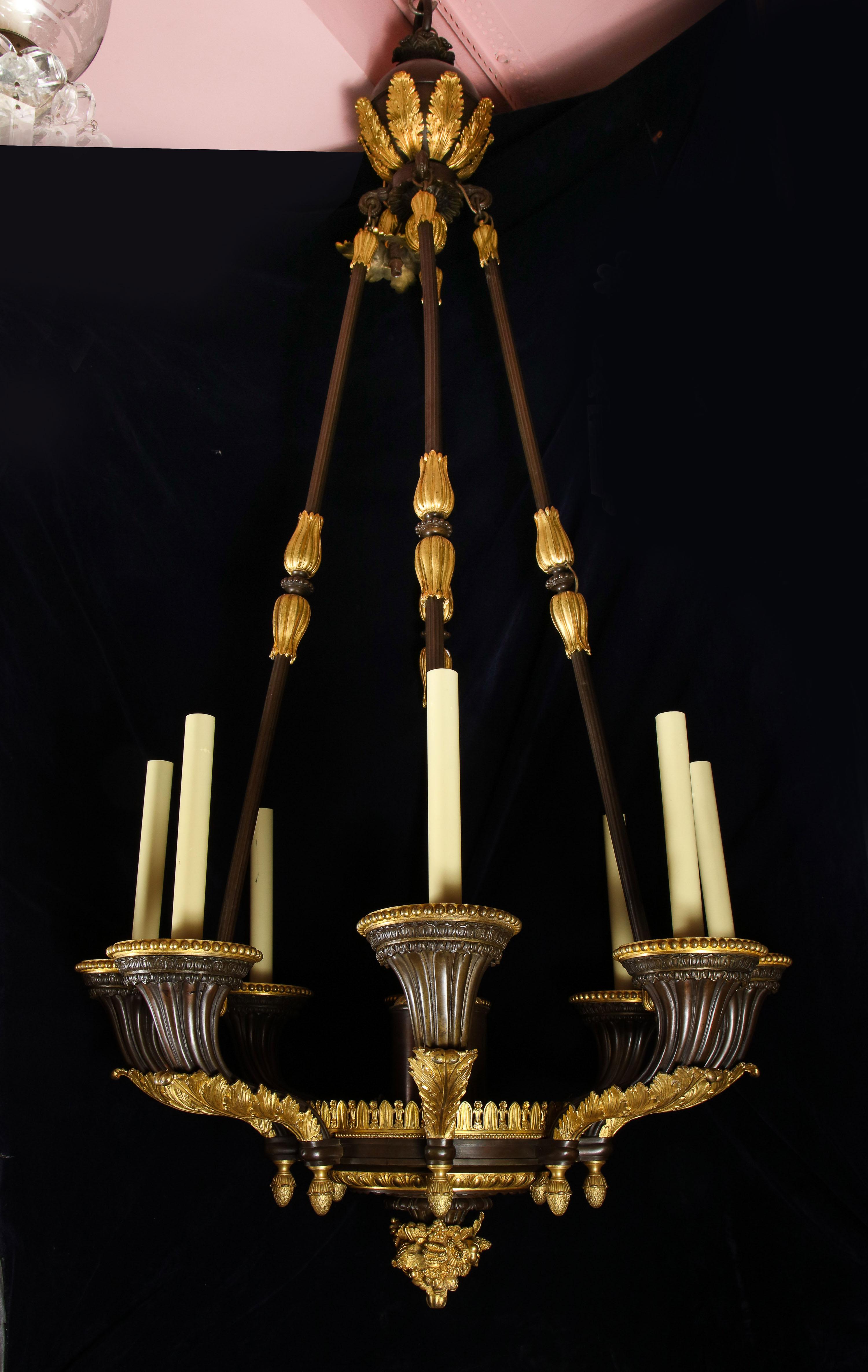 A monumental and unique antique French Empire neoclassical gilt bronze and patinated bronze multi light chandelier of superb quality and detail. This large chandelier is embellished with the most unusual large thick heavy arms, bronze rods which are