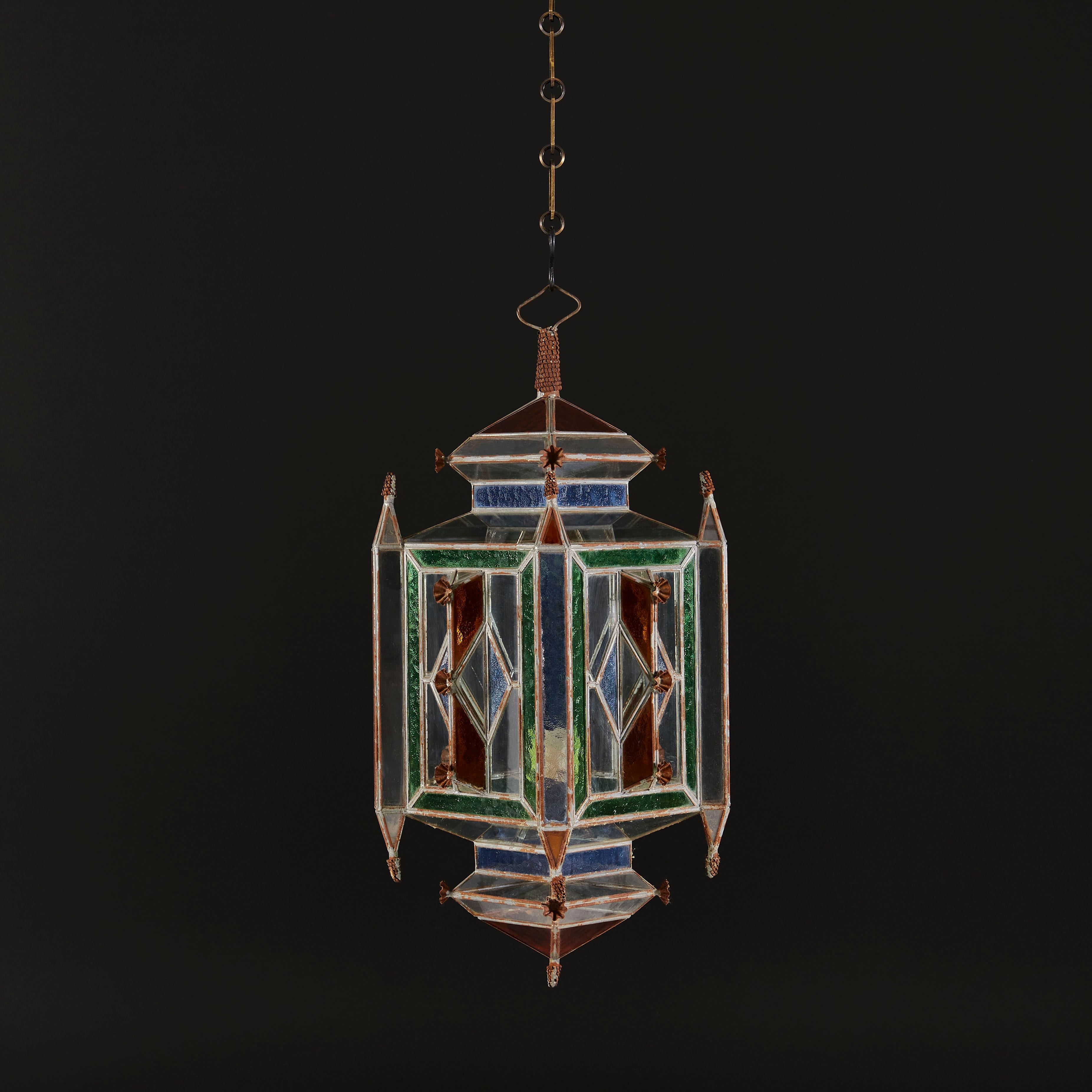 An early twentieth century Moorish hanging lantern with metal frame incorporating mounted flowers and finials to the top and bottom of the corners. With blue, green, amber and clear glass inset panels.

Currently wired for the UK. Please enquire for