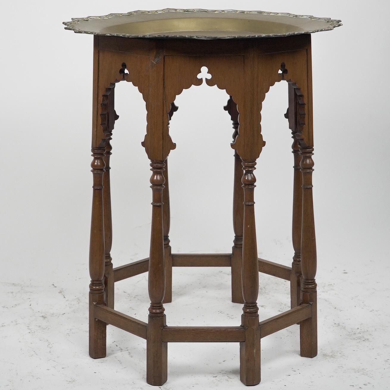Liberty & Co style. 
A Moorish-style side table with a heavy brass removable dish-shaped table top, richly engraved with floral decoration to the wavy edge and a bird of paradise to the centre, with Moorish arched aprons on six turned legs united by