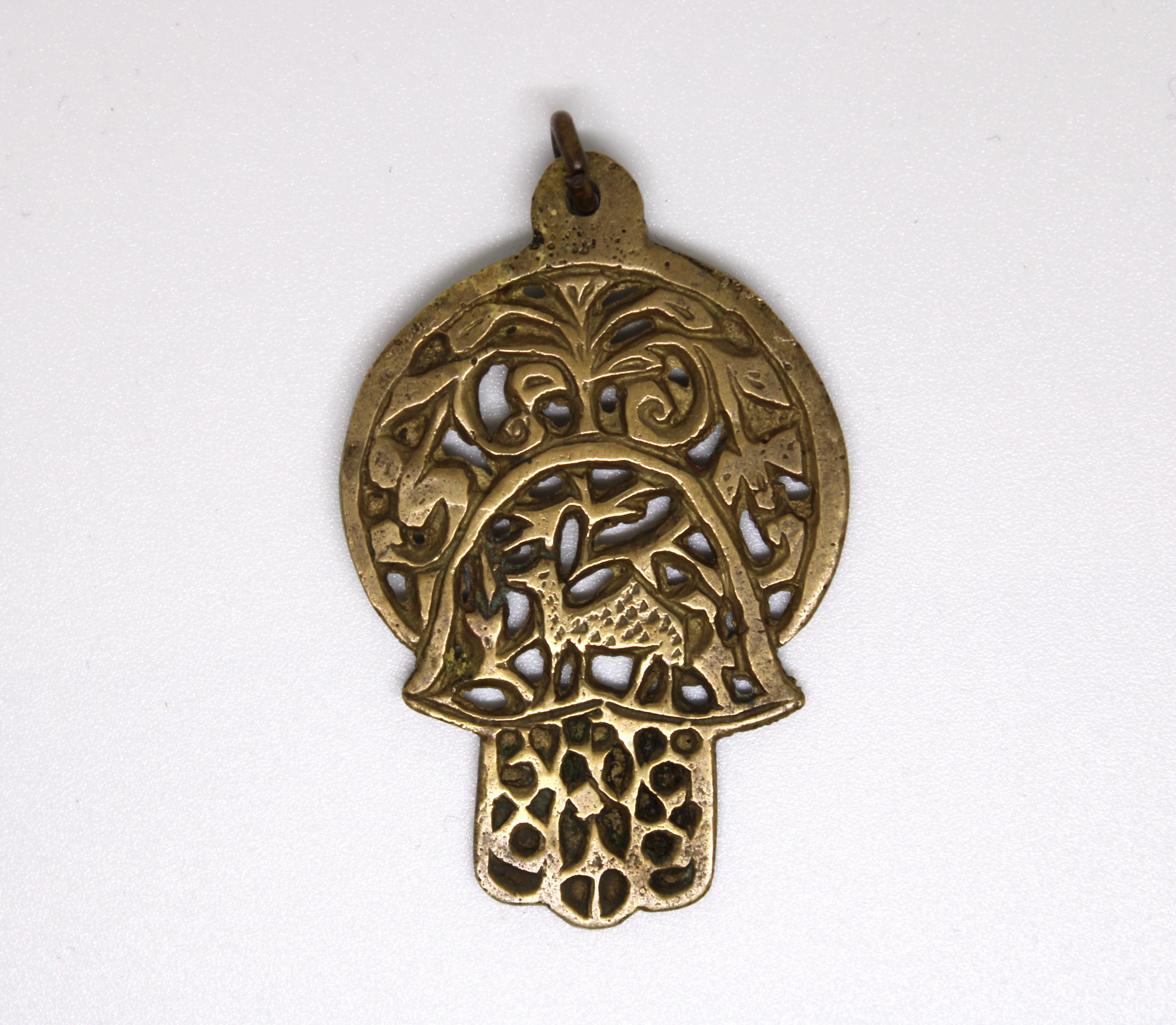 Cette magnifique amulette Hamsa, fabriquée au Maroc au début du XXe siècle, témoigne du riche patrimoine artistique de l'Afrique du Nord. Façonnée dans un laiton chaud et vieilli, cette pièce présente un magnifique design ajouré, incorporant