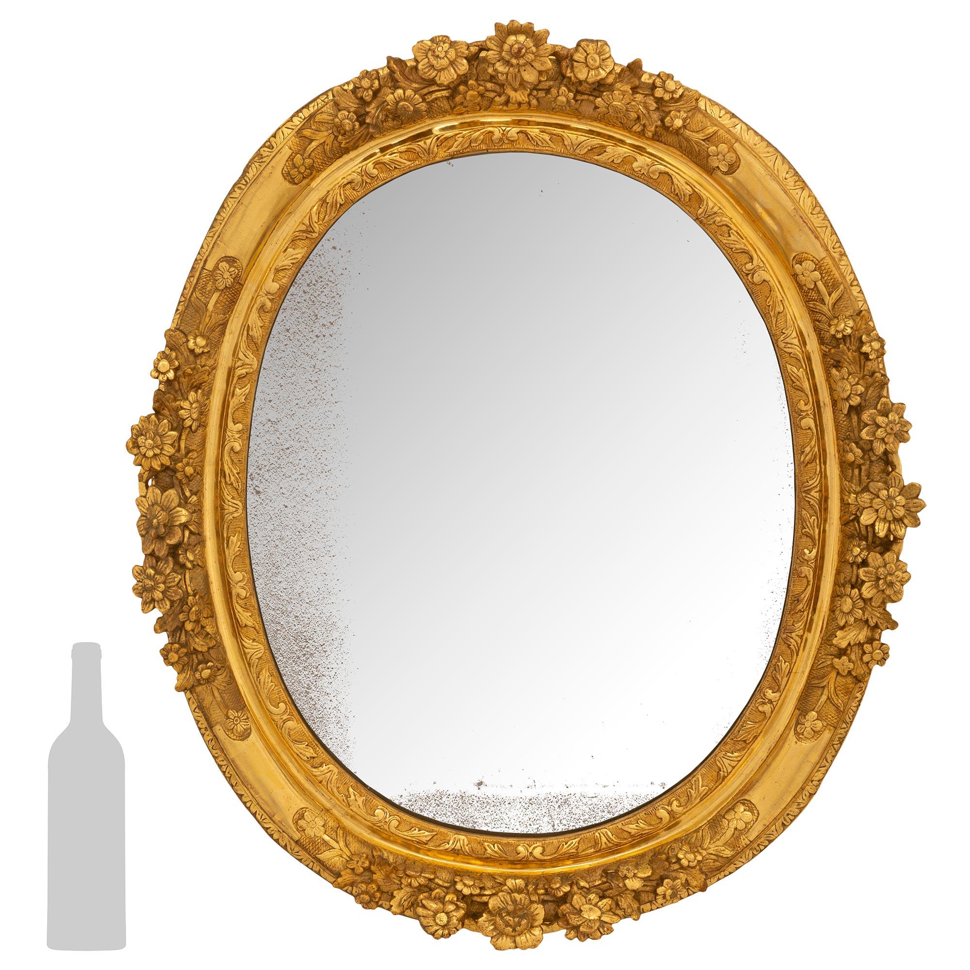 A stunning French 18th century Louis XIV Period finely carved giltwood mirror. This oval mirror has an interior scrolled designed border and large protruding carved foliate frame with acanthus leaf designed trim. With all original mirror plate and