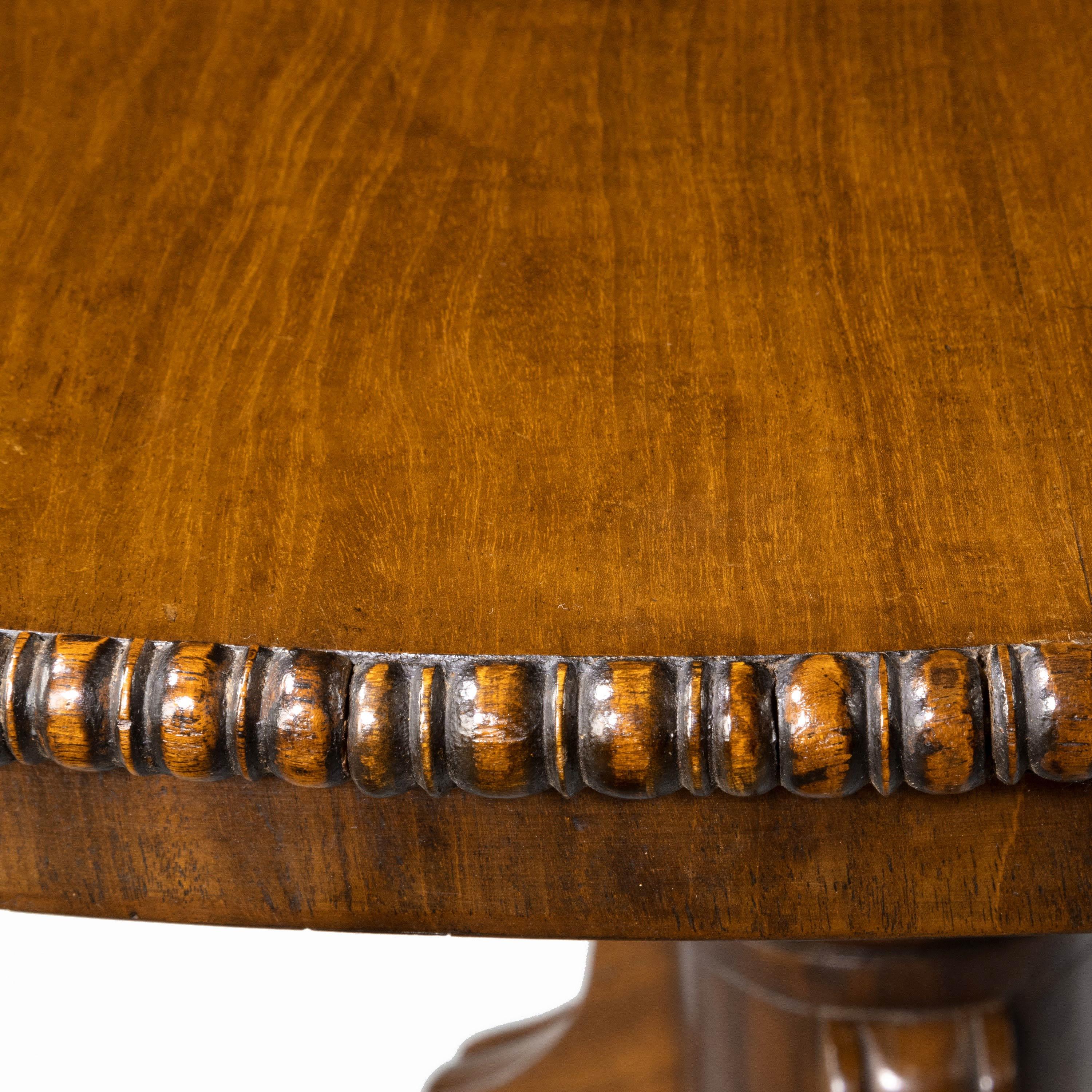 A most attractive Regency period tilt-top dining table. With finely figured timbers on a well turned central stem over three high swept nickel reeded supports. Retaining the original shoes and castors. The original snap mechanism to the top.