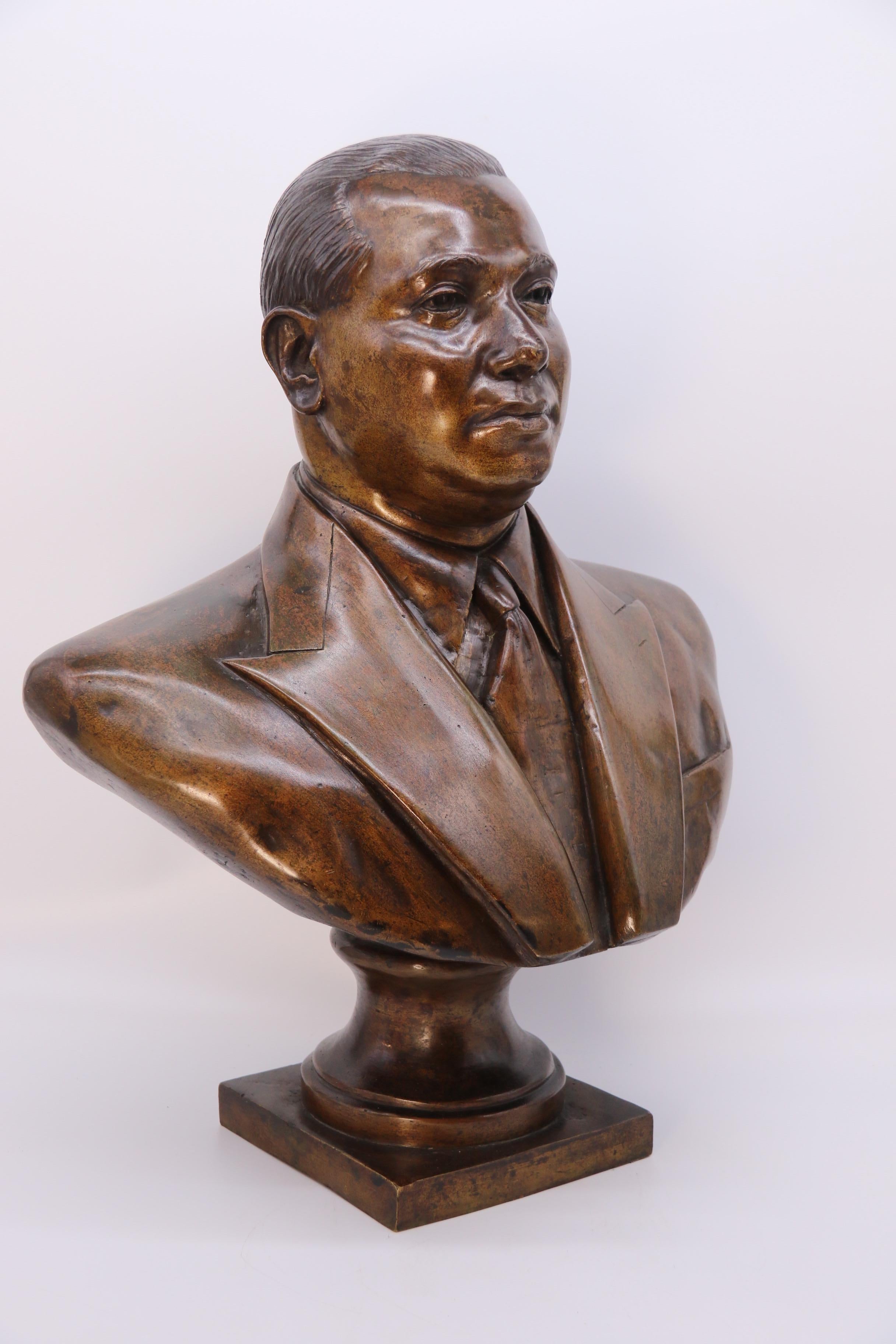 This most unusual almost life sized heavily cast bronze bust depicts a very smart most likely South American gentleman dressed in a double breasted suit jacket with a shirt and tie. He is a relatively young man with strong handsome features and a