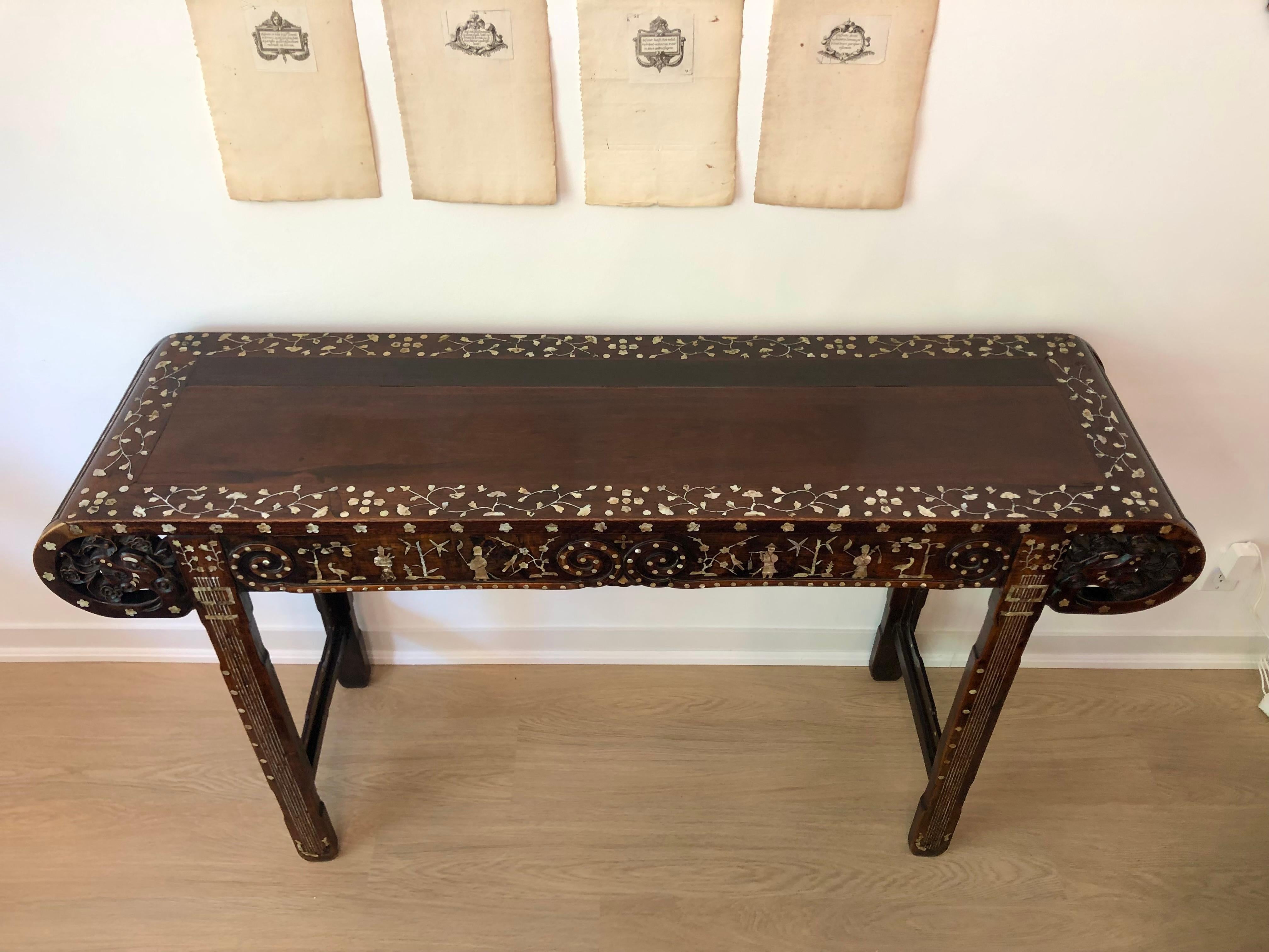 This is a gorgeous late Qing Dynasty Chinese altar table made of Rosewood. Scroll ends carved with dragons and beautiful mother-of-pearl inlay on all sides, including top, back, legs and even inner rails. The top inlaid with a border of scrolling