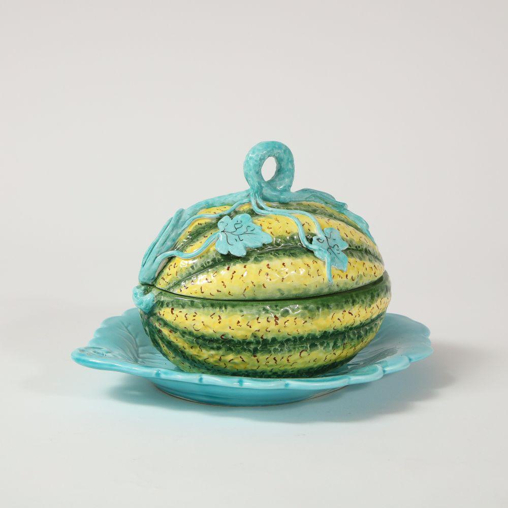 The tureen in the form of a yellow and green-striped squash with a turquoise scrolling vine surmounting the lid; with turquoise foliage-form underdish. The underside with Mottahedeh sticker and bearing number and 