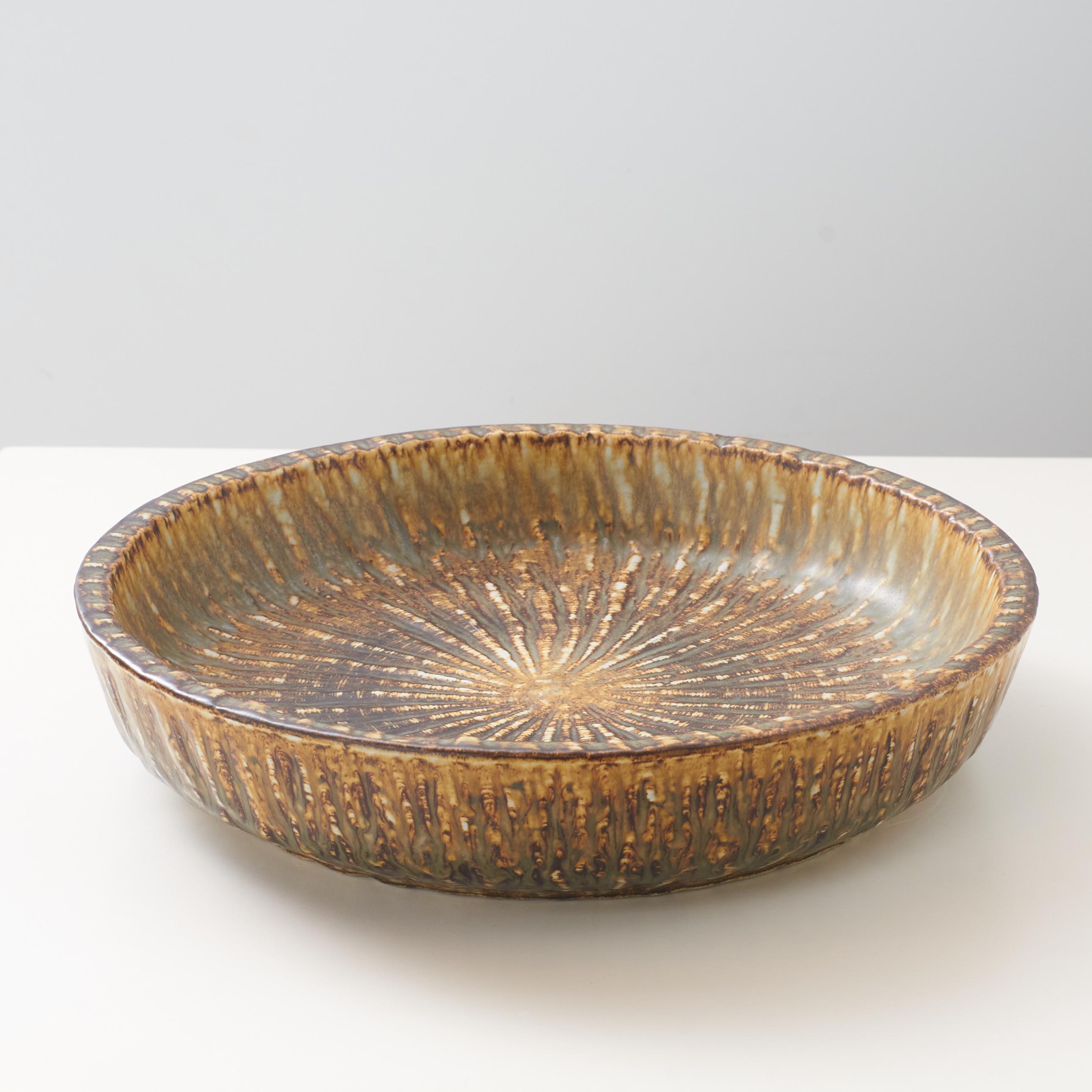 A mottled brown and yellow deep sided round shaped ceramic dish by Gunnar Nylund for Rorstrand. Rebus Series #8.
Inscribed on the bottom with the makers and the manufacturer’s mark.