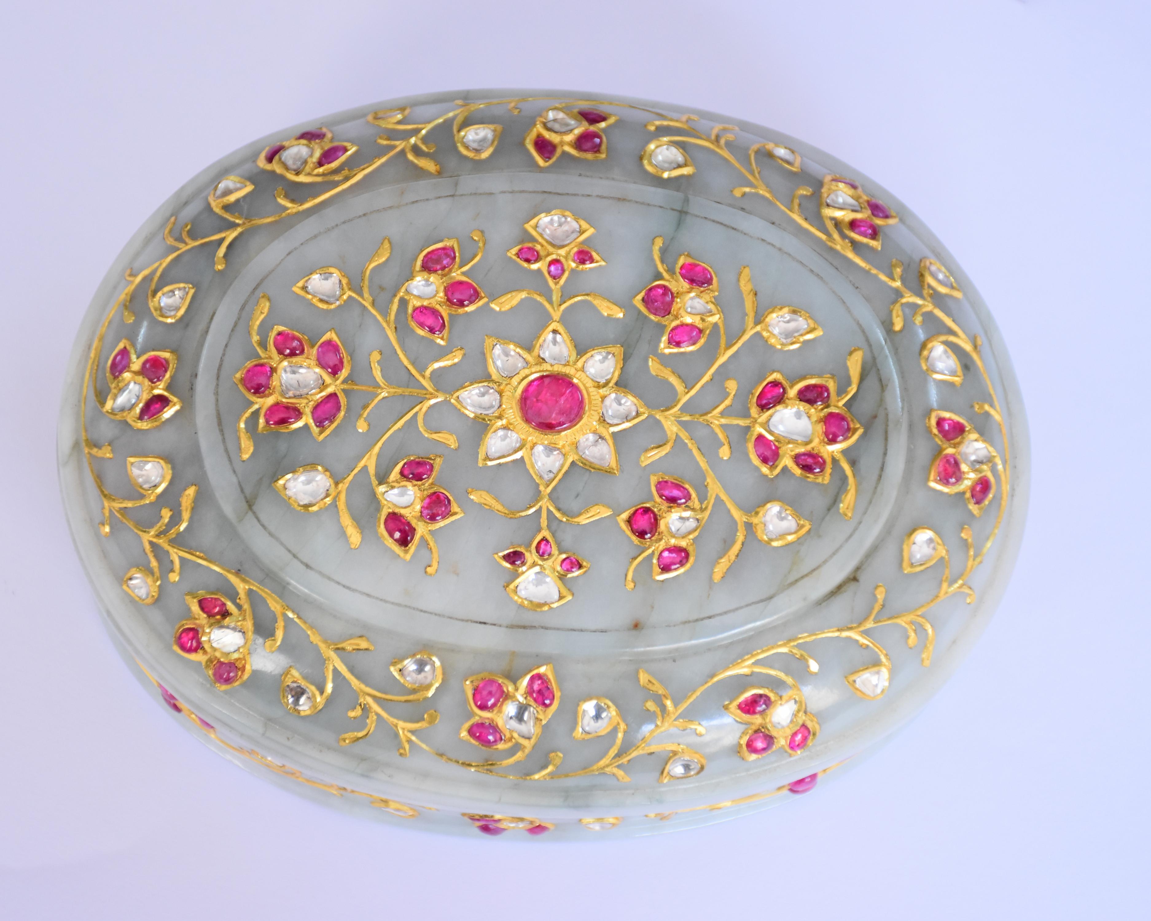 Engastada con rubíes birmanos naturales, polkis de diamantes y oro, esta caja de jade de jadeíta de forma ovalada está decorada con talla mogol en la parte posterior. La caja está expertamente tallada y ahuecada por dentro con paredes rectas, que