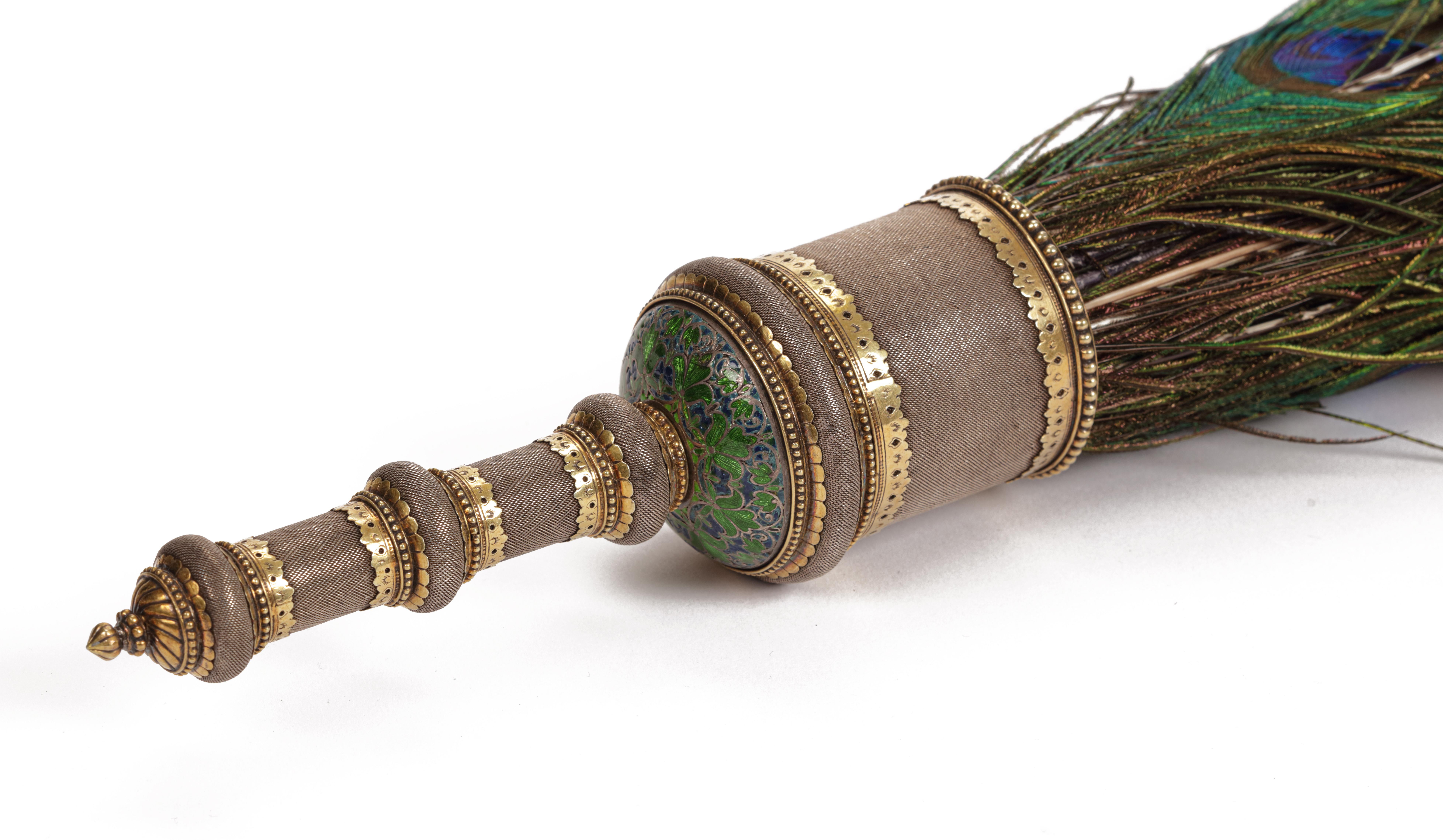 India, probably Deccan, 2nd half 17th century

L. 121 cm (overall) / L. 17.5 x Diam. 5.5 cm (handle)

The magnificent silver, silver-gilt and enamelled peacock feather fan (morchal), composed of a cylindrical silver core encased in very fine silver