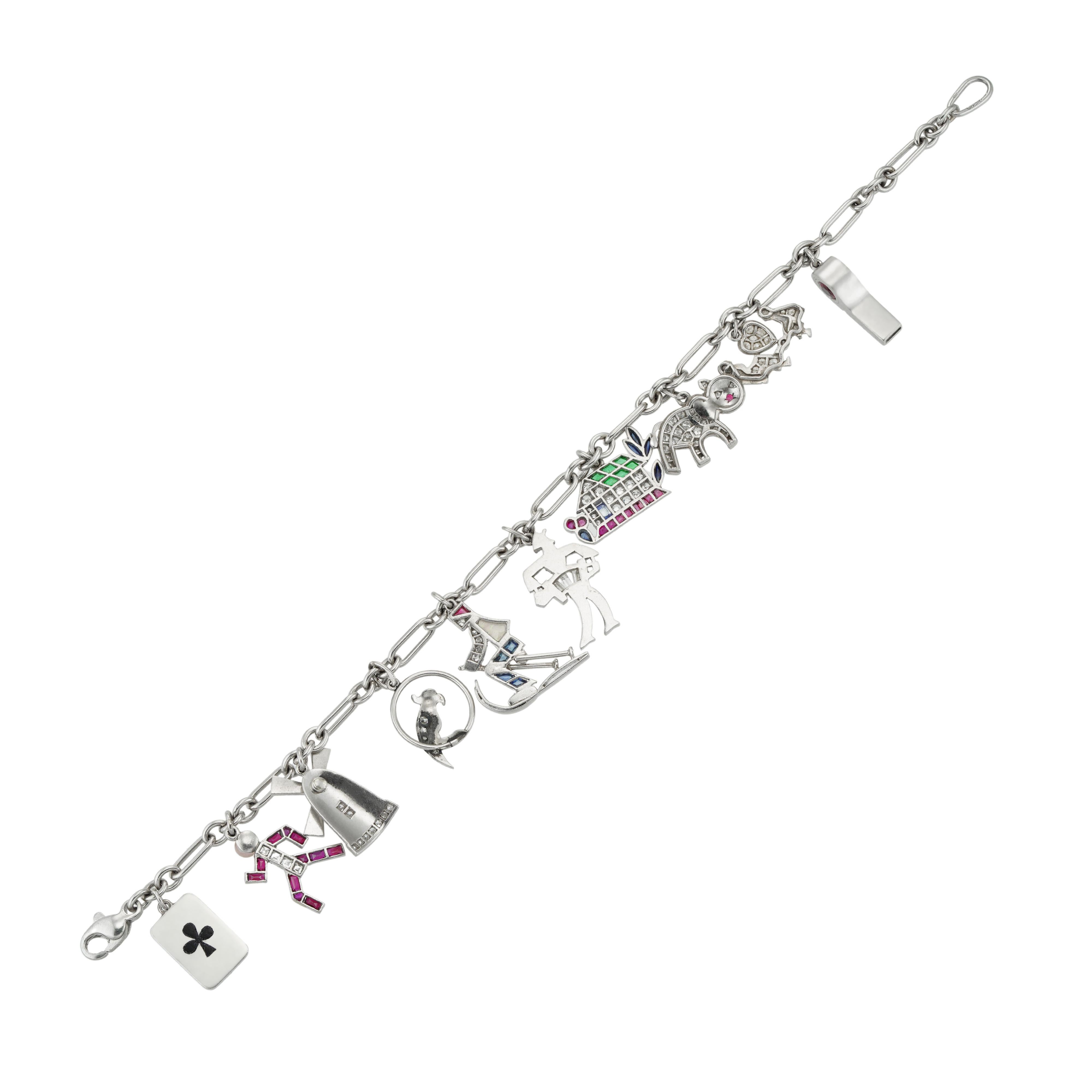 A multi gem-set charm bracelet, the fetter link platinum chain, supporting ten charms, each depicting a different subject, including a whistle, a couple on a see-saw, a cat, a house, a man playing an accordion, a skier, a parrot perched on a ring, a