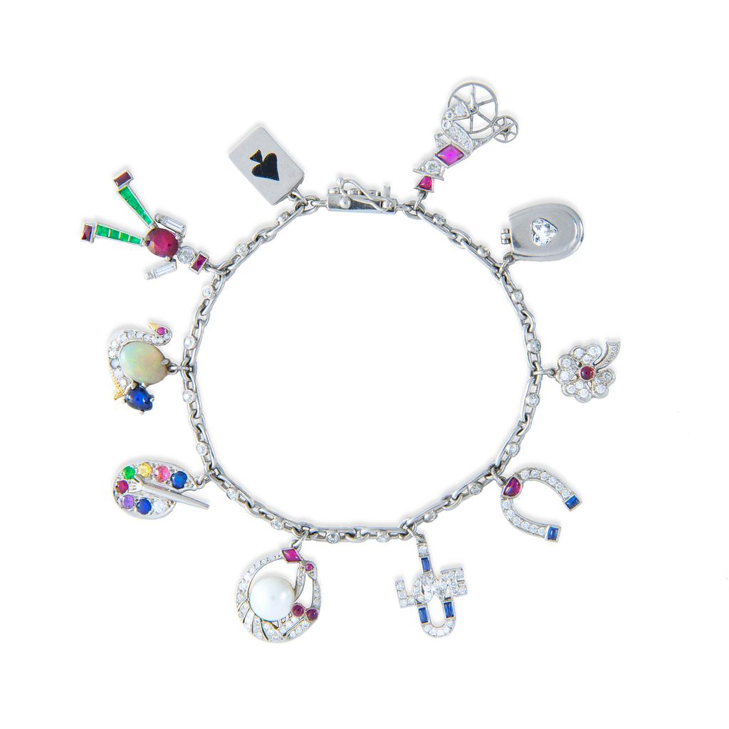 A multi gem-set charm bracelet, the fetter link platinum chain millegrain rub-over set with twenty-one  round brilliant-cut diamonds, estimated to weigh a total of 1.0 carat, suspending ten charms, each depicting a different subject, a card