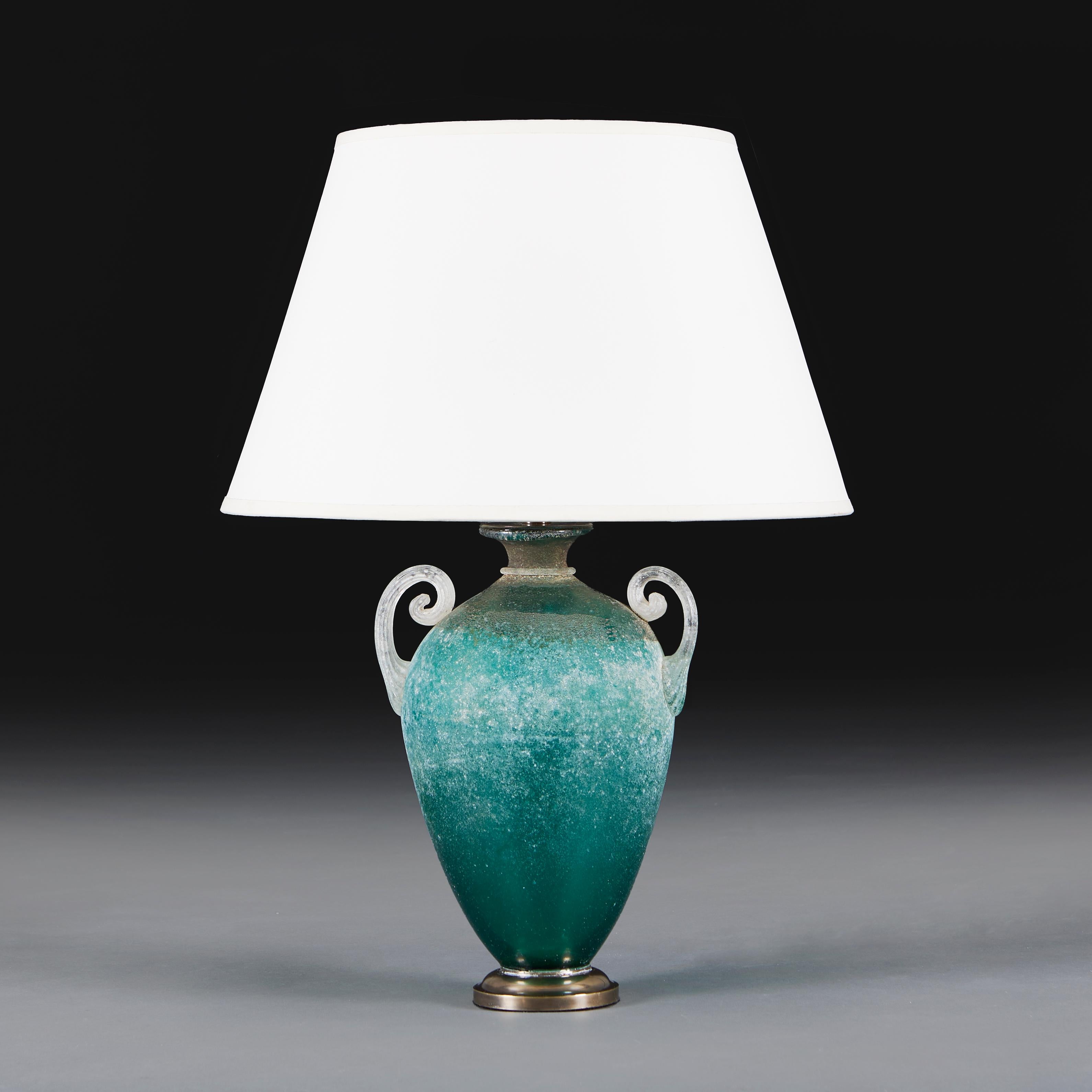 A mid-20th century Murano amphora vase, with finely modelled handles and mottled decoration. Now mounted as a lamp on a turned patinated brass base.

Please note:
Lampshade not included. Lamp photographed with a 16” diameter pale cream card Pembroke