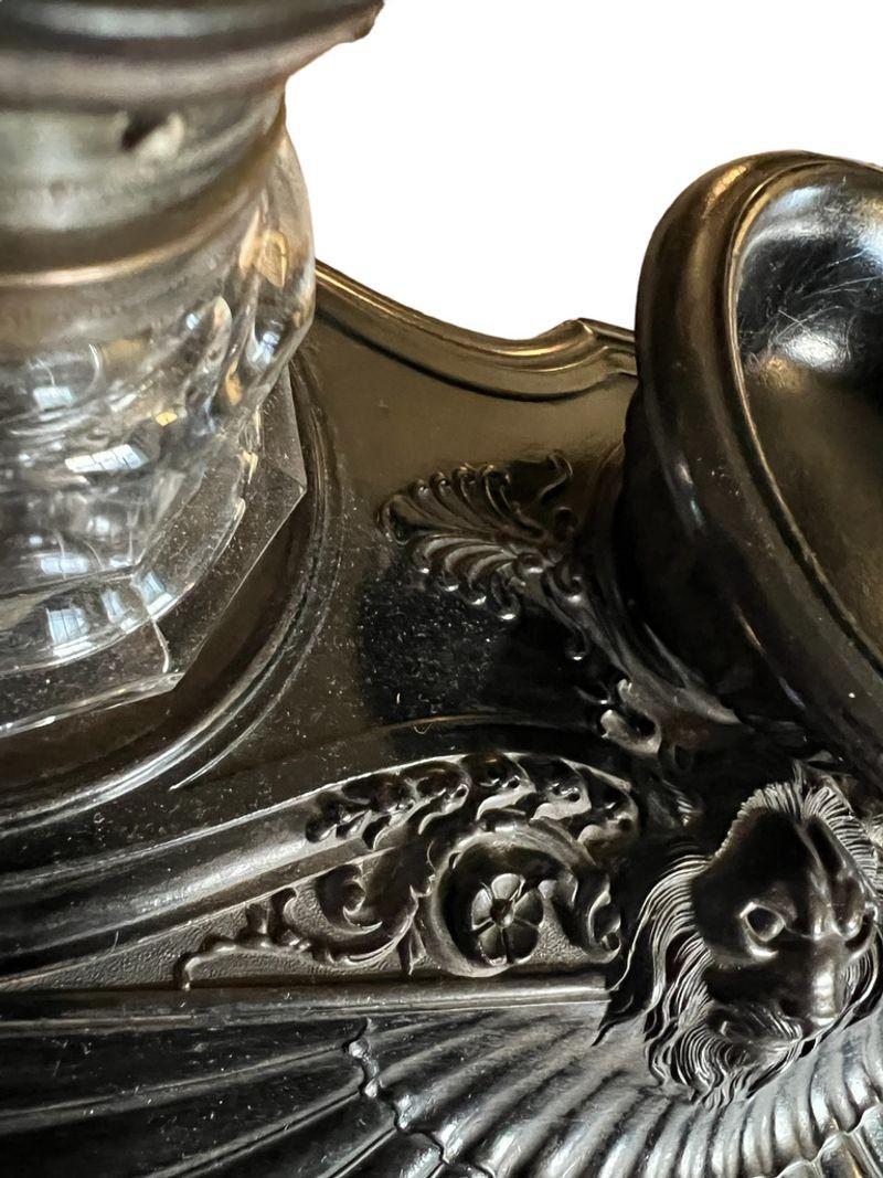 The black inkstand with a molded lion decoration with a shell pen tray. The two glass inkwells on either end.