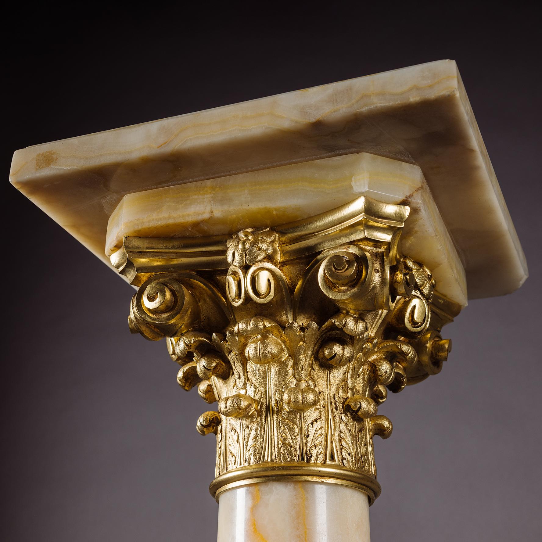 A Napoleon III Gilt-Bronze and Algerian Onyx Pedestal.

Of classical form, the pale figured onyx column with square section platform top with moulded edge, above a finely cast gilt-bronze Corinthian capital and laurel banded socle, raised on a