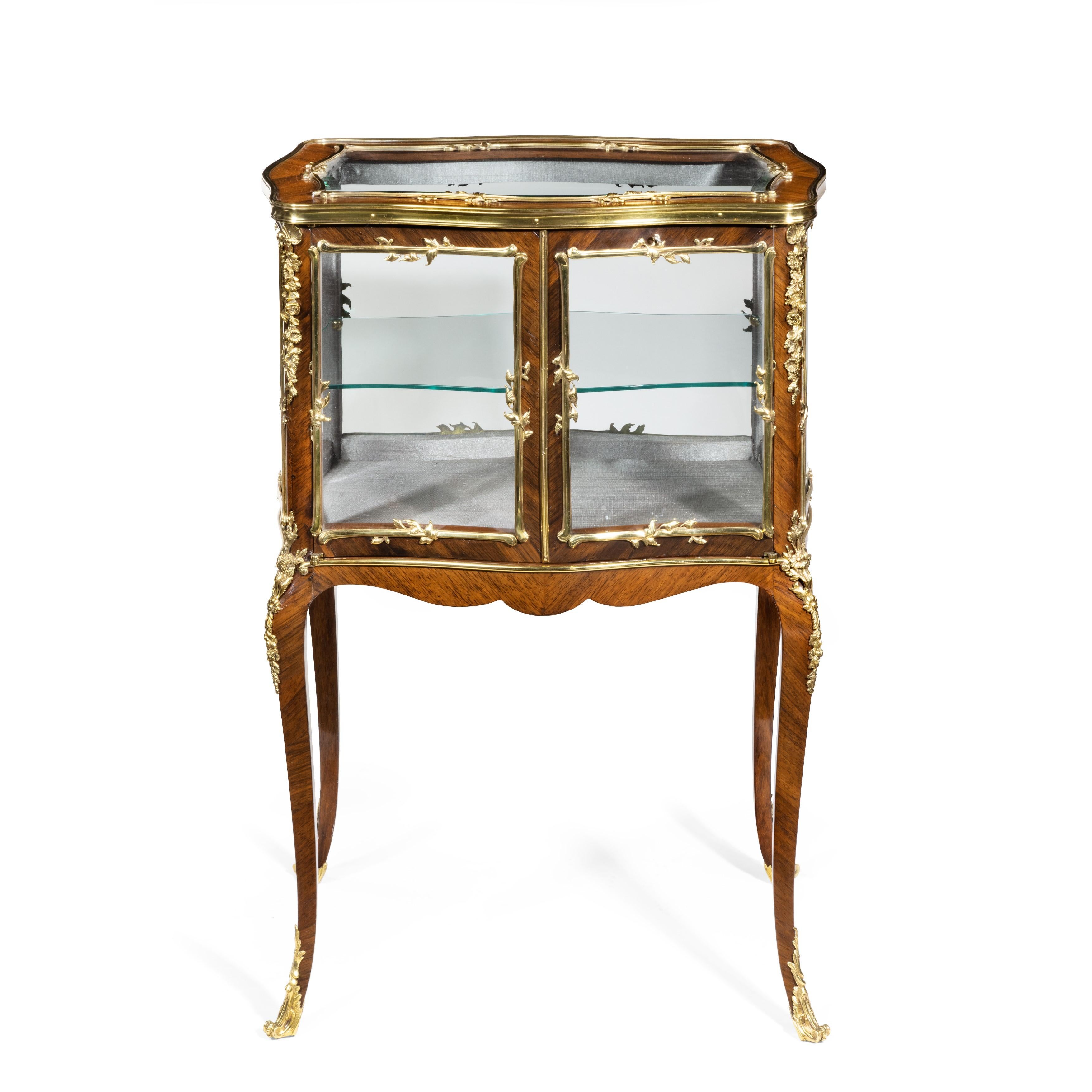 A Napoleon III kingwood bijouterie table, of serpentine rectangular form with a glass top, shelf and sides, with two doors to the front, raised on slender cabriole legs, decorated throughout with cross banding and fine quality ormolu mounts of
