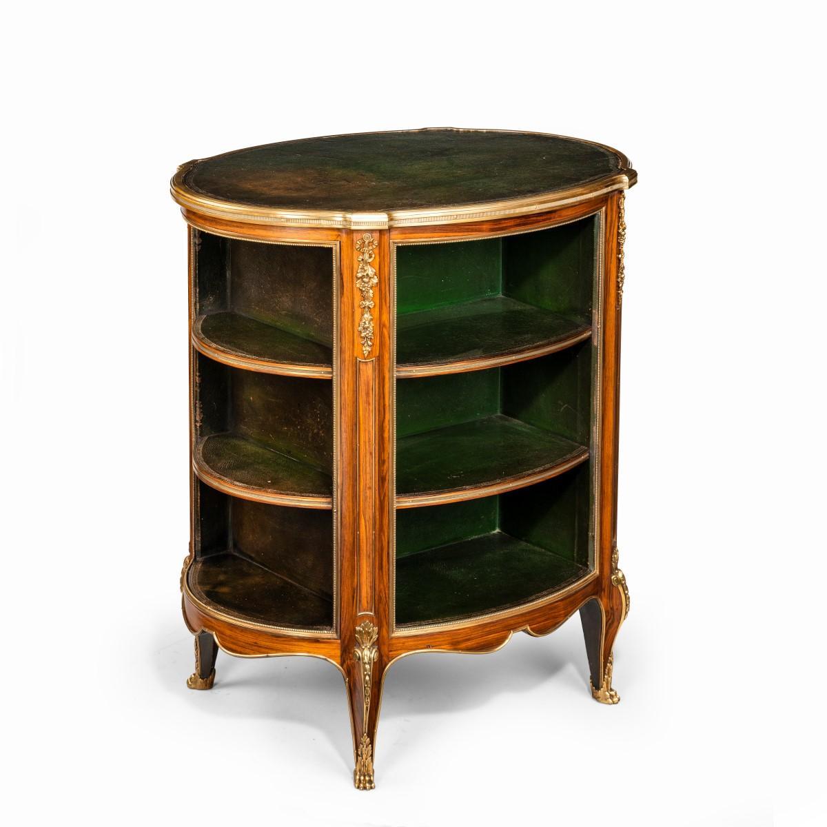 A Napoleon III kingwood freestanding open bookcase, of oval form with four angled, fluted pilasters, the top and three shelves covered with tooled green leather, applied with moulded ormolu edging and ribbon-tied garlands, all raised on cabriole