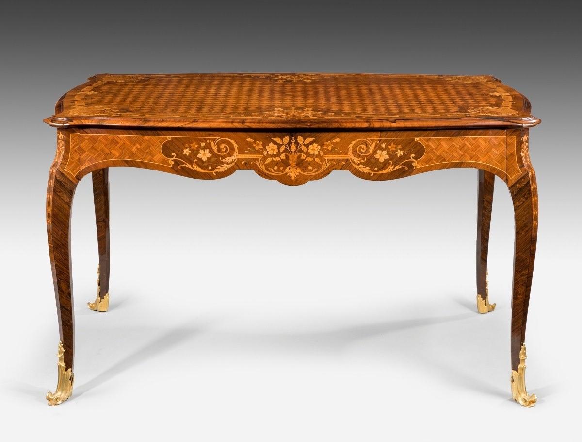 A Napoleon single drawer kingwood library table, decorated in marquetery and parquetry inlays, the shaped top with a diamond trellis field within a border of flowers and vases, the frieze with a disguised drawer on one side decorated with further