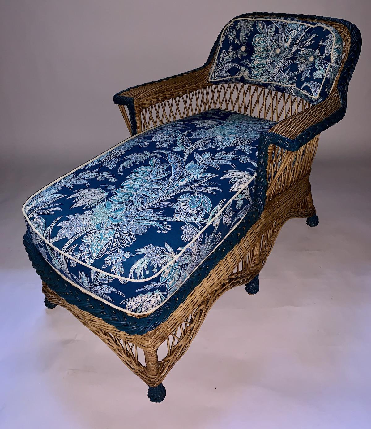 A beautiful reed and rattan wicker chaise lounge in a lovely natural color with a continuous navy blue braid trimming around the back, arms and seating, American, C. 1910 by the Heywood Wakefield Company of Gardner Ma. The perfect piece for your