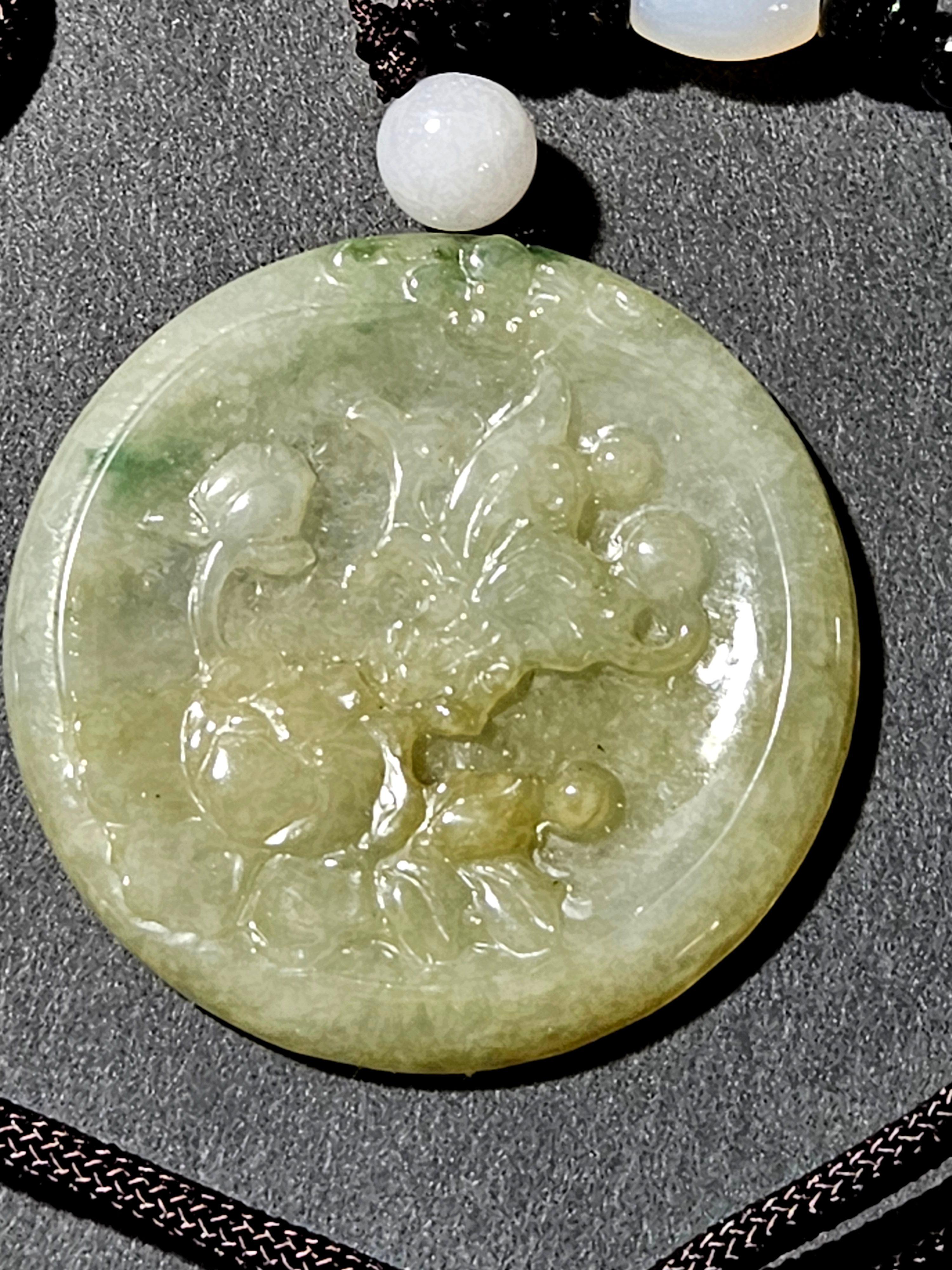 Pendentif disque en jadéite naturelle du Myanmar Ric#JD004 dans sa boîte en bois. Les couleurs semblent être le blanc, le jaune clair et le vert, et la sculpture en relief présente un motif floral.