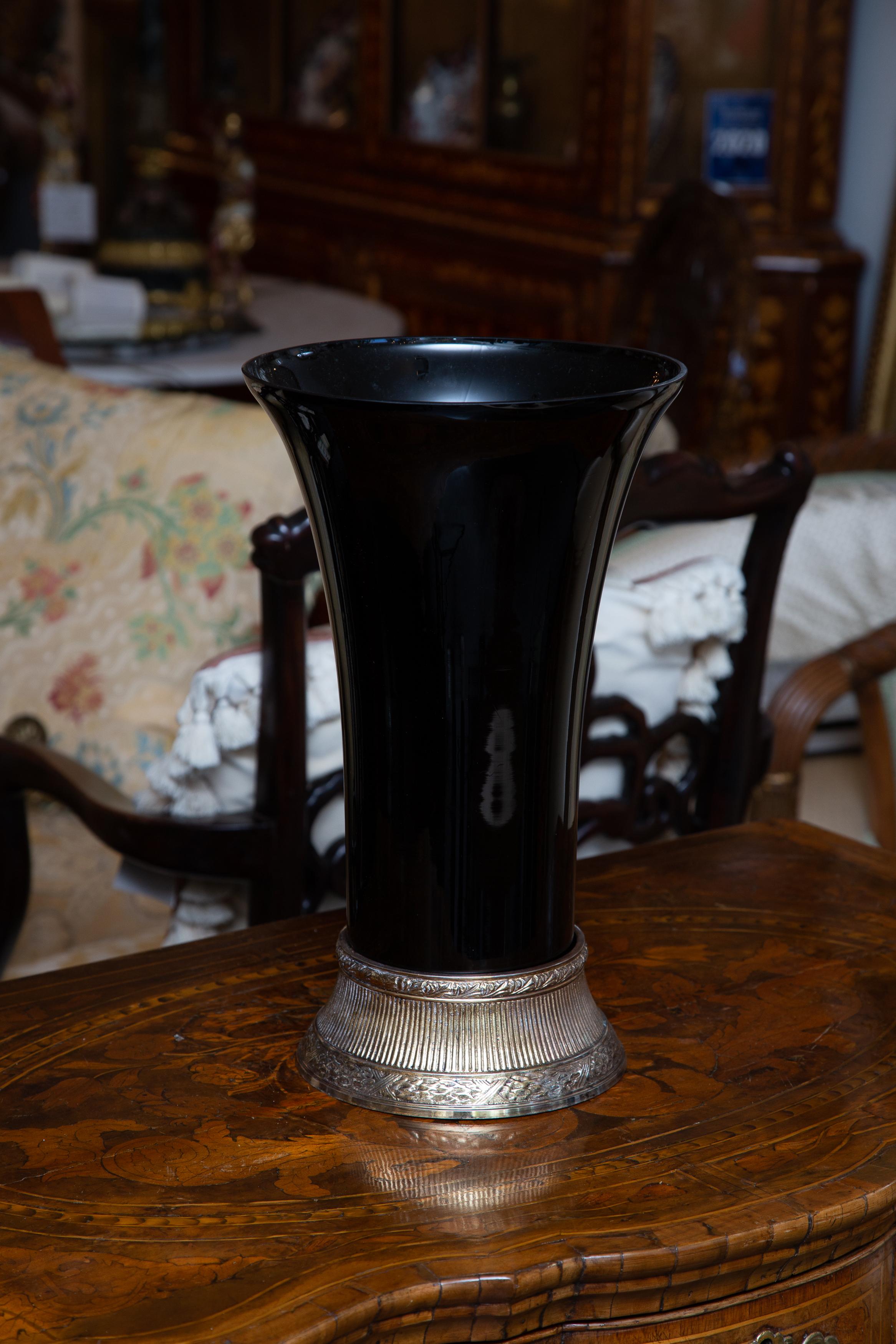 This is a sophisticated near-pair of Art Deco style black glass vases situated on silvered metal bases, 20th century. The larger vase is 8.75 inches in diameter and 14.5 inches high. The slightly smaller vase is 8.33 inches in diameter and 14 inches