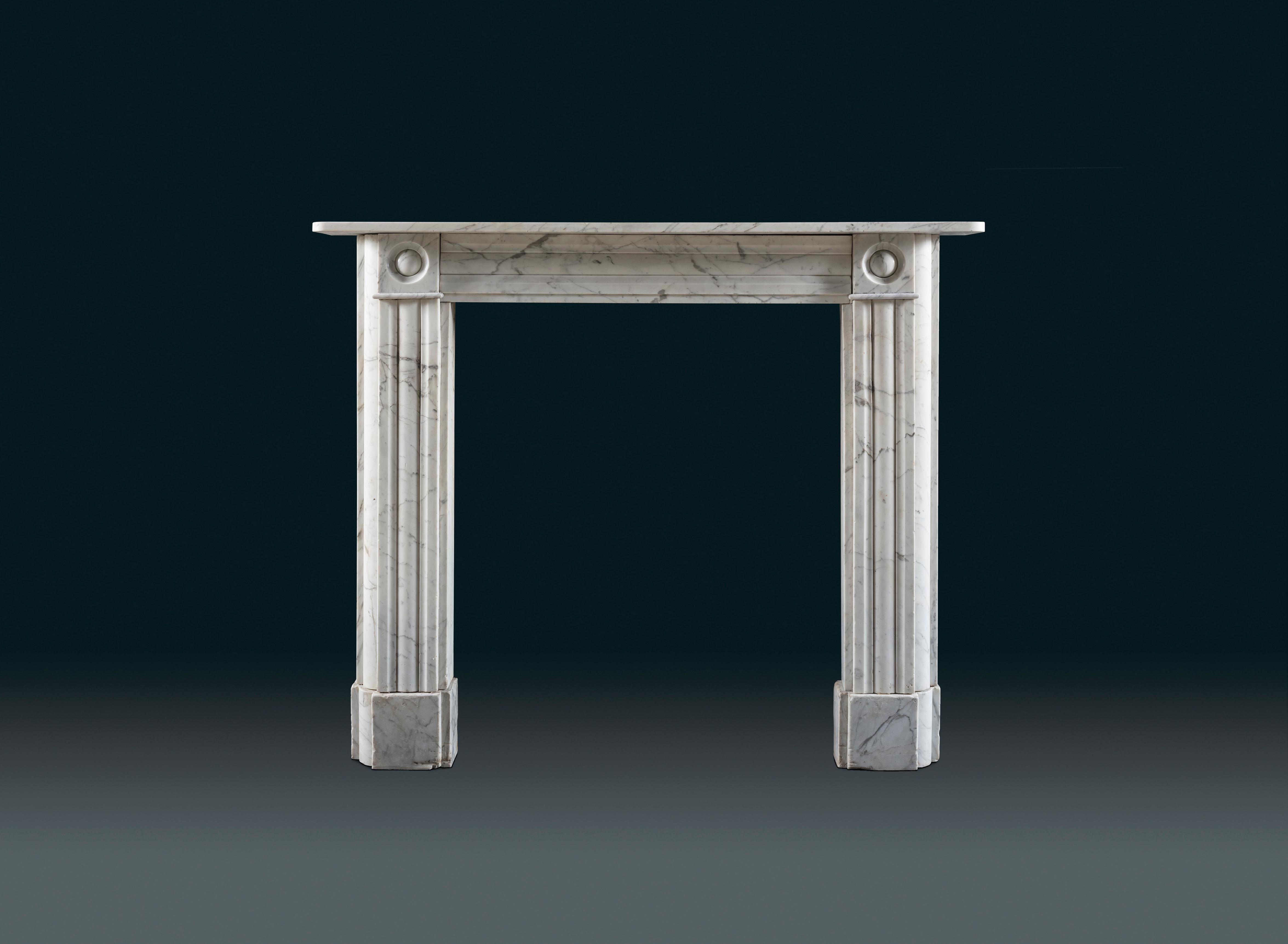 A near pair of classic Regency Bullseye chimneypiece of gracious proportions carved in Carrara marble.
The simple shelf sits above finely carved bullseye end-blocks, flanking a plain panelled frieze and supported by rounded, reeded jambs.
Both