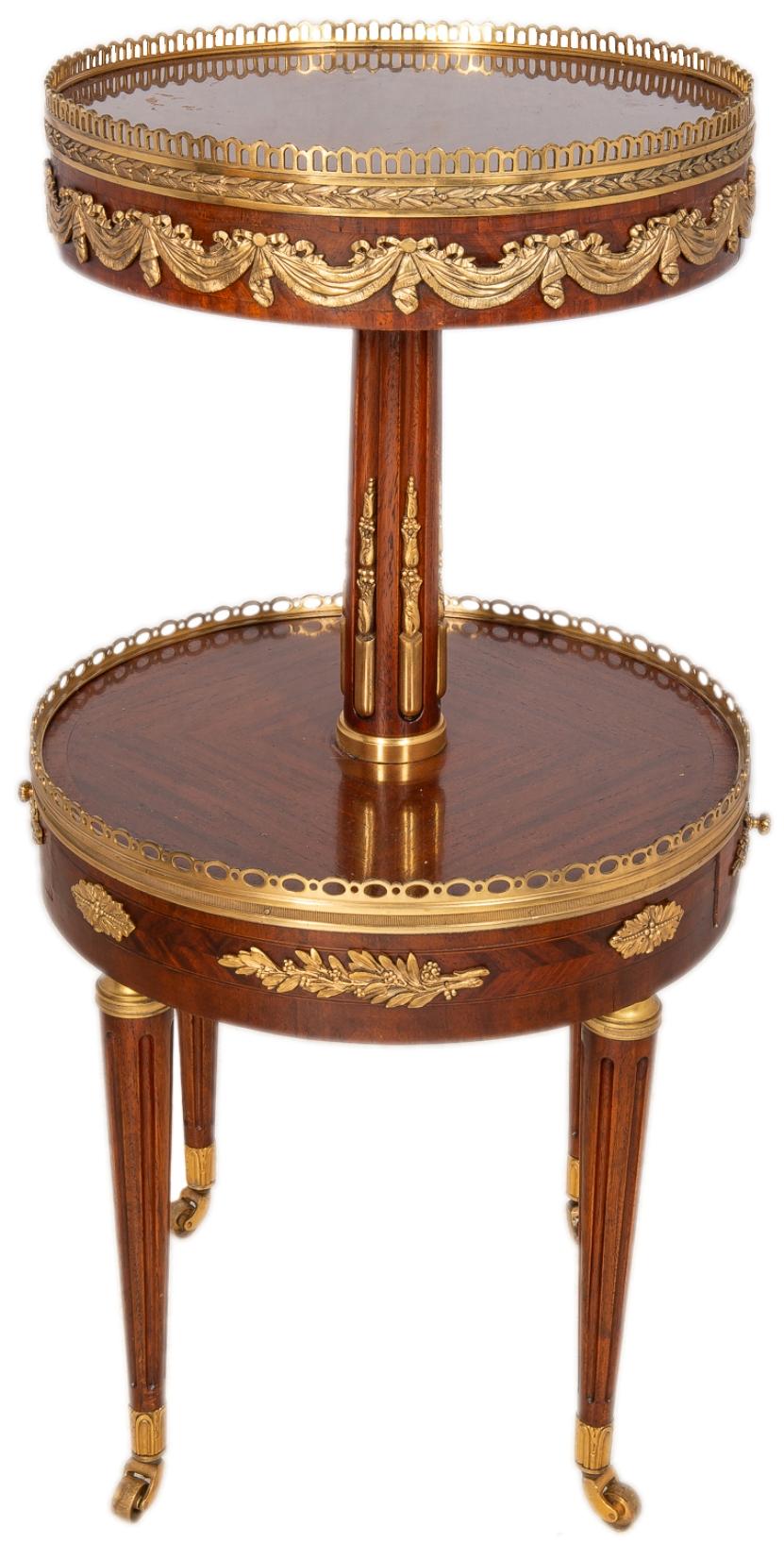 A good quality near pair of French Louis XVI style Mahogany two-tier circular side tables, each with gilded ormolu mounts, galleries to both tiers, a frieze drawer and raised on turned tapering fluted legs terminating in brass castors.