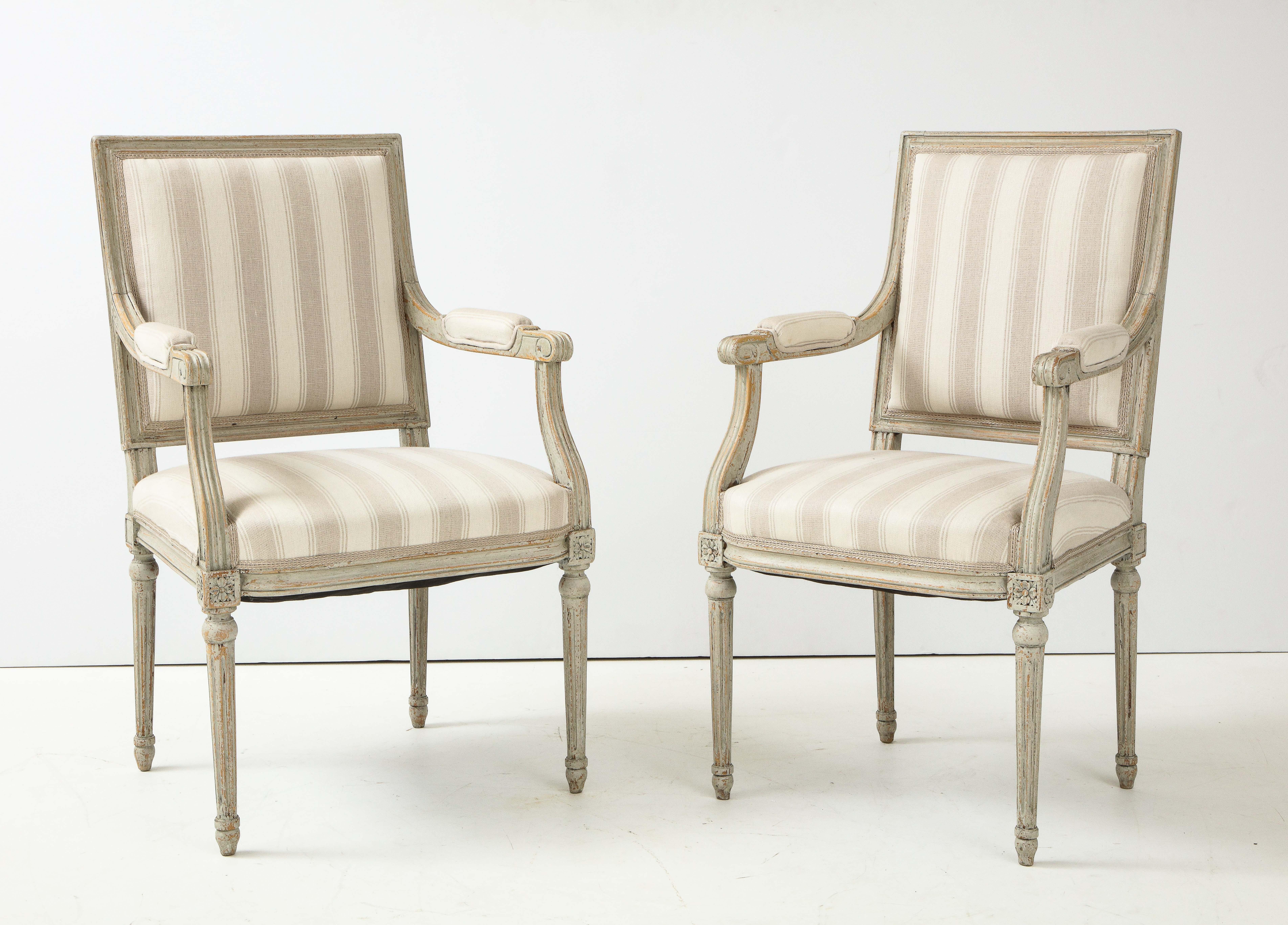 A near pair of Swedish Late Gustavian style painted open armchairs, Late 19th Century, with rectangular upholstered backrests, straight partially padded armrests raised on carved scale supports, upholstered seats raised on circular tapered and