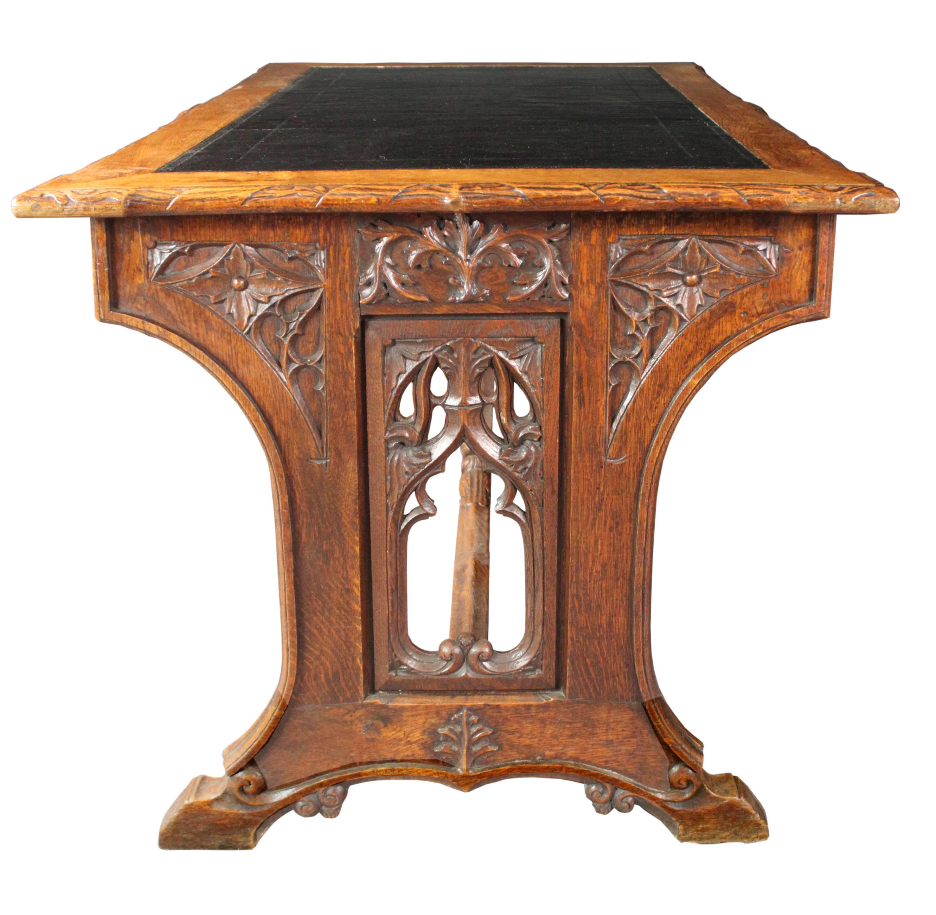 A rare neo-Gothic writing table with superb carved detail mainly in a foliate design: striking pointed-arch pierced ends and carved stretcher, knobs and escutcheon; the rectangular top with carved edges and an inset black leather; good original