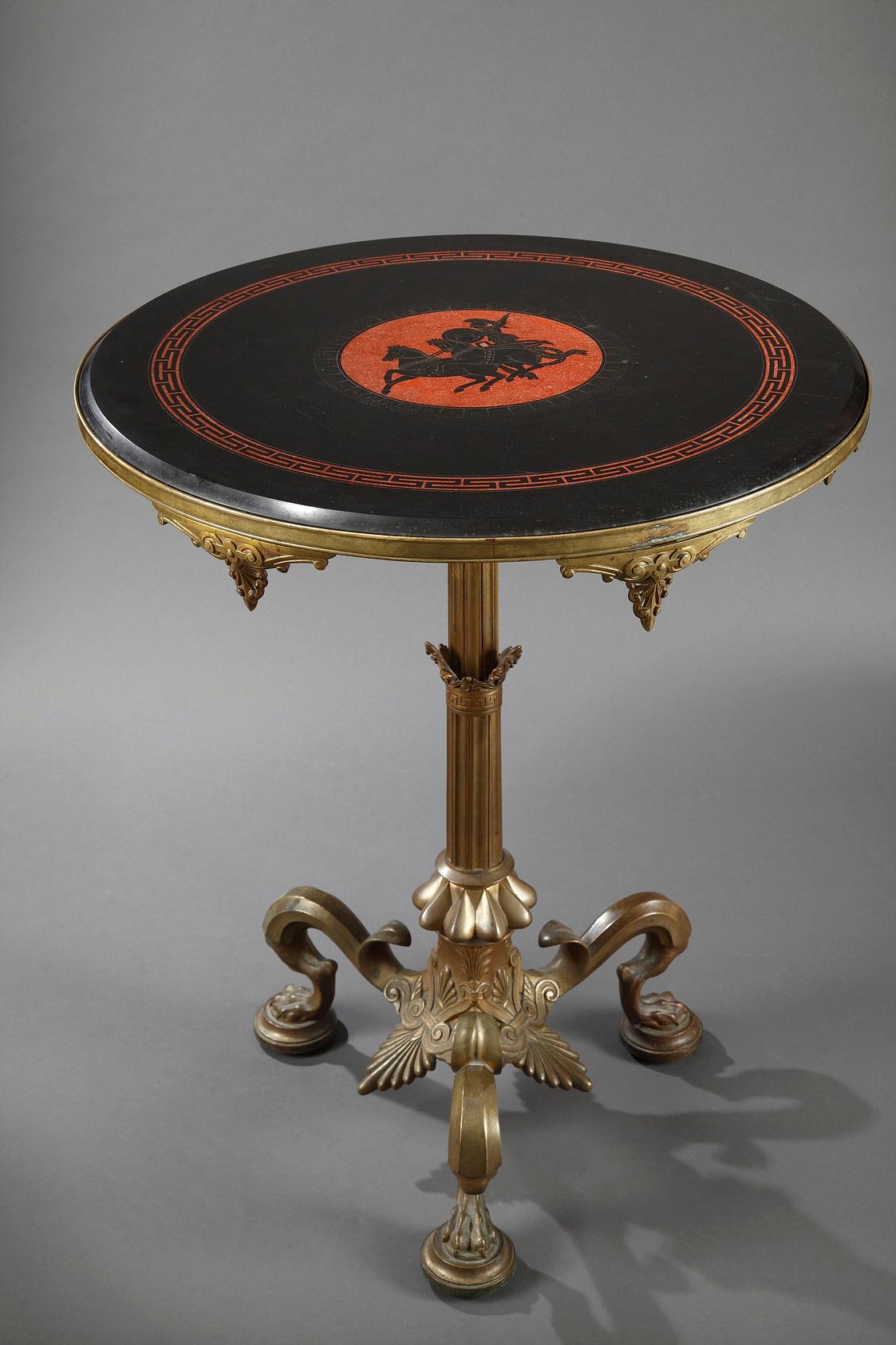 A tripod gueridon in gilded bronze attributed to F. Barbedienne, decorated with palm-leaves and standing on lion’s feet. The black marble top is decorated with an antique chariot scene and a Greek frieze picked out in red « Pompeian »