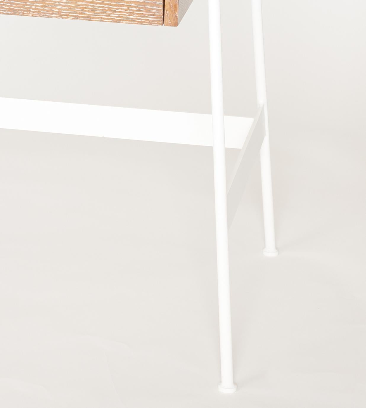 Un nouveau bureau en chêne cérusé de style midcentury avec un tiroir flottant à droite de la partie inférieure avec une tirette en cuir d'origine et soutenu par quatre pieds en fer évasés reliés par une traverse en forme de H revêtue de poudre
