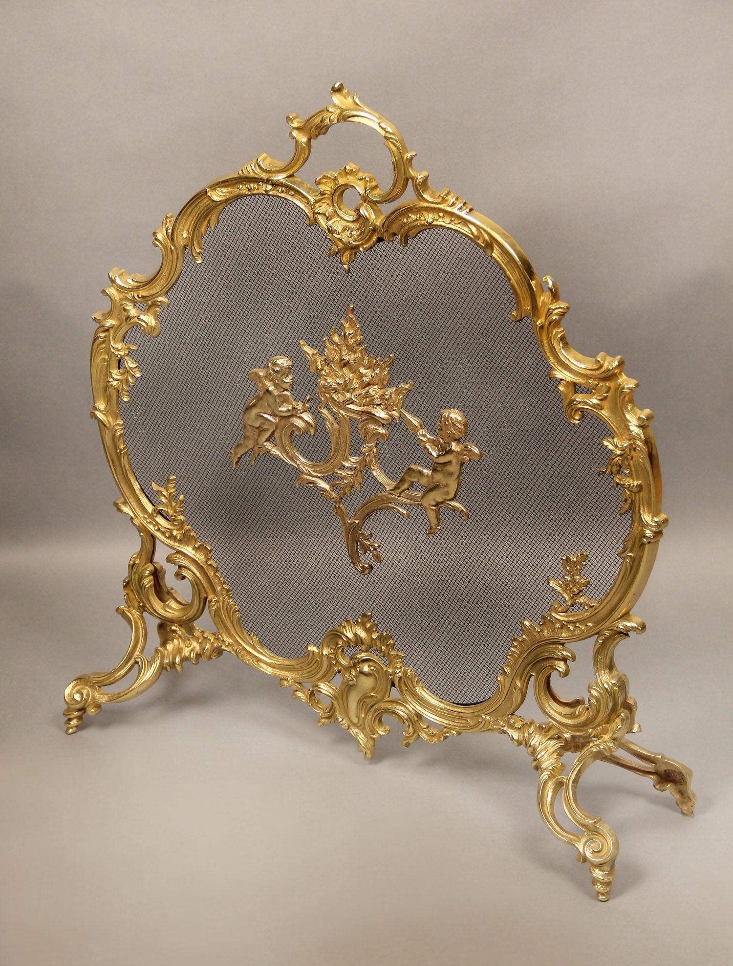 A Nice late 19th century gilt bronze firescreen

The Rococo oval shaped scrolling bronze frame centered with cherubs fanning a flame, standing on four spiral feet.
